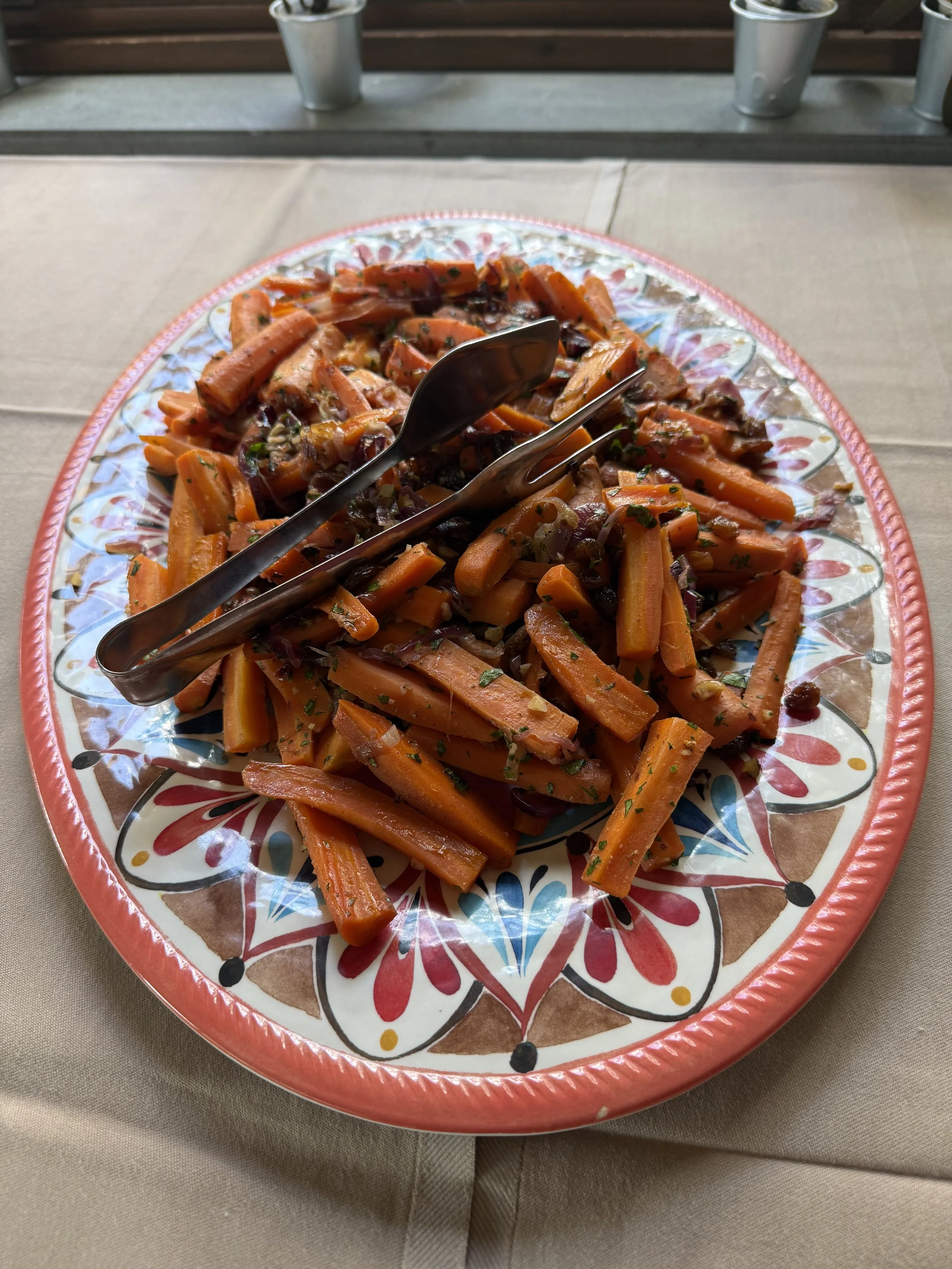 A colorful, decorative plate with cooked carrots garnished with herbs, placed on a beige tablecloth.