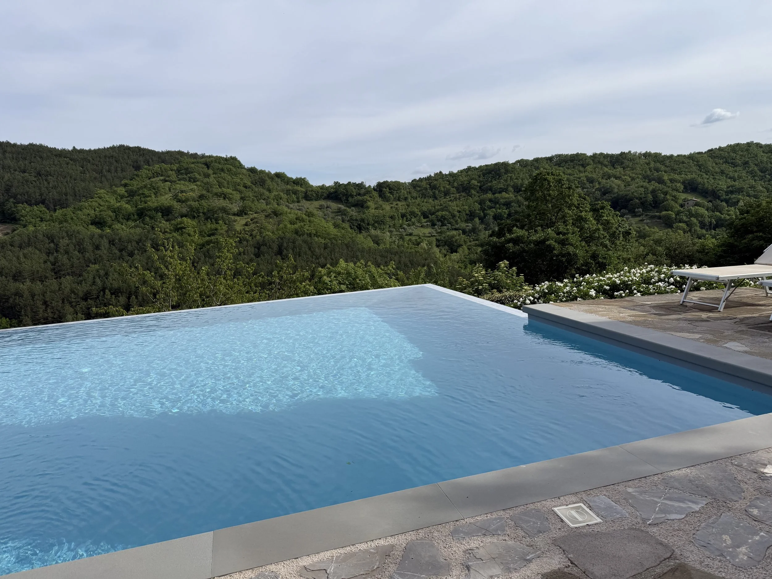Swimming pool with blue water overlooking green hills and cloudy sky.