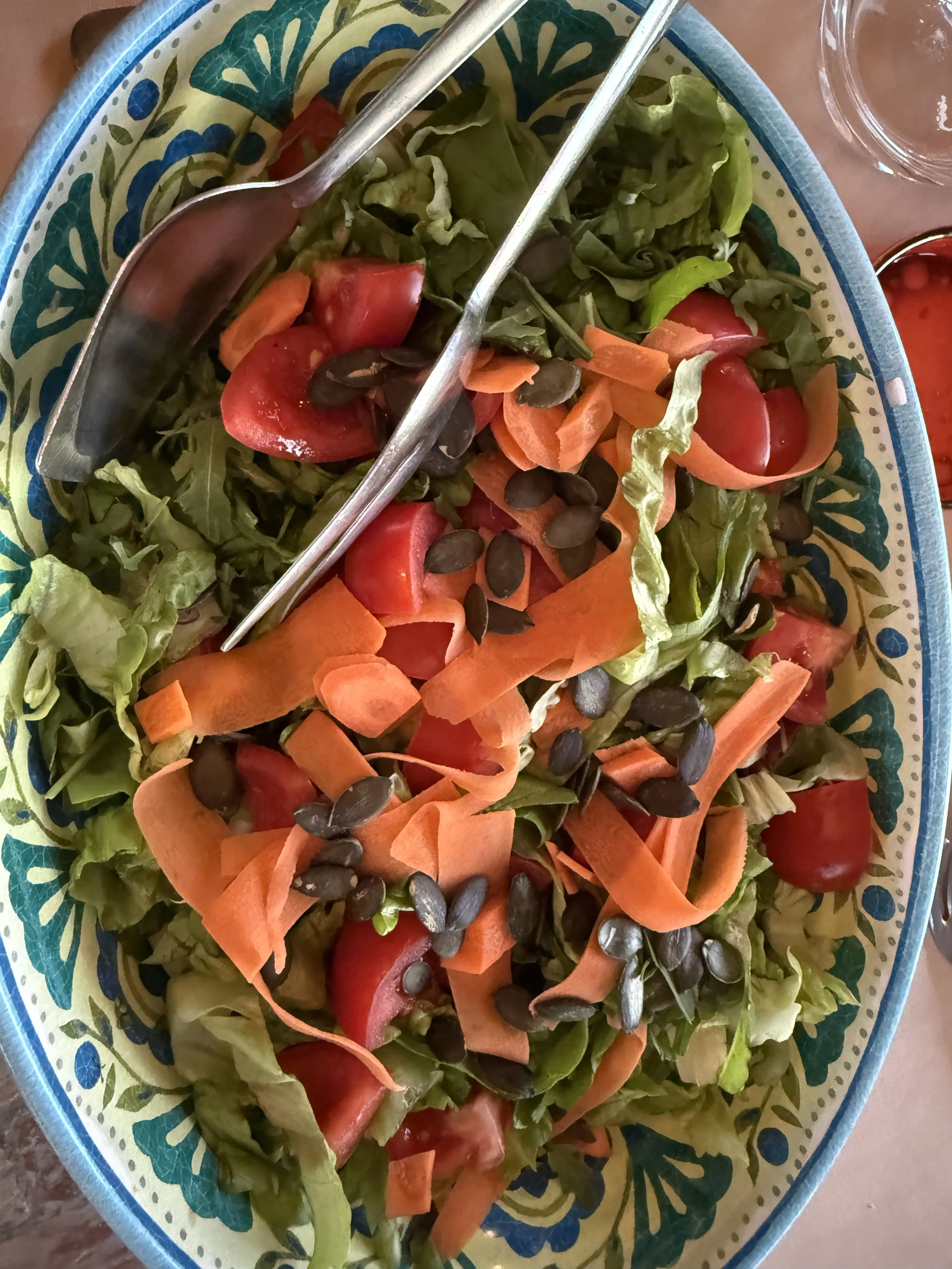 A salad in a colorful ceramic bowl with leafy greens, cherry tomatoes, shredded carrots, black beans, and salad tongs.