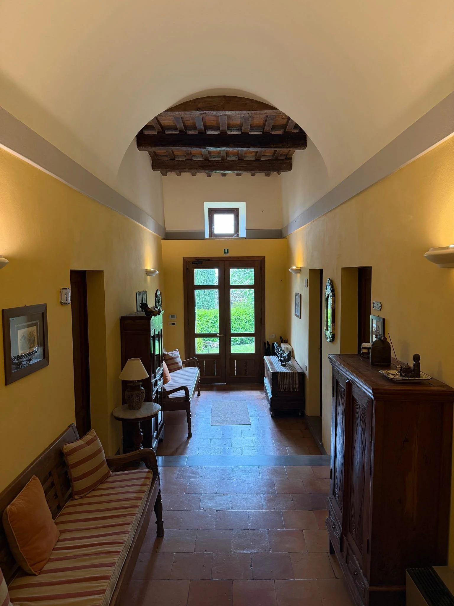 Hallway with yellow walls, wooden furniture, a small window, wooden ceiling beams, and a tiled floor.