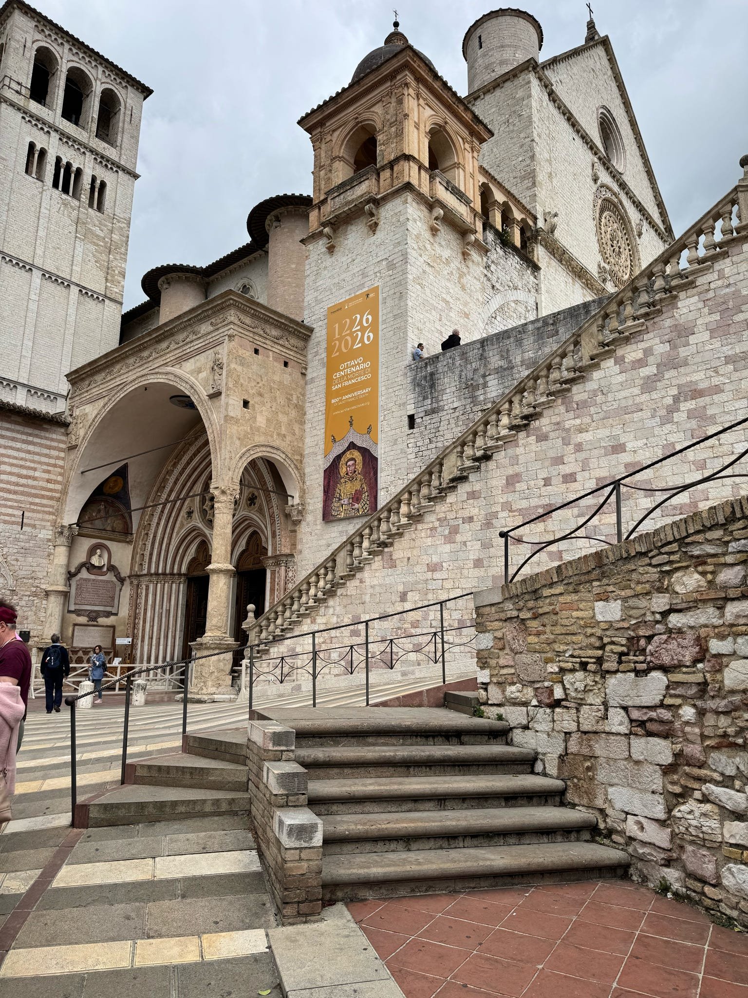 Exterior view of a historic stone church with a large rose window and a bell tower, with expressive architecture and visitors at the entrance.