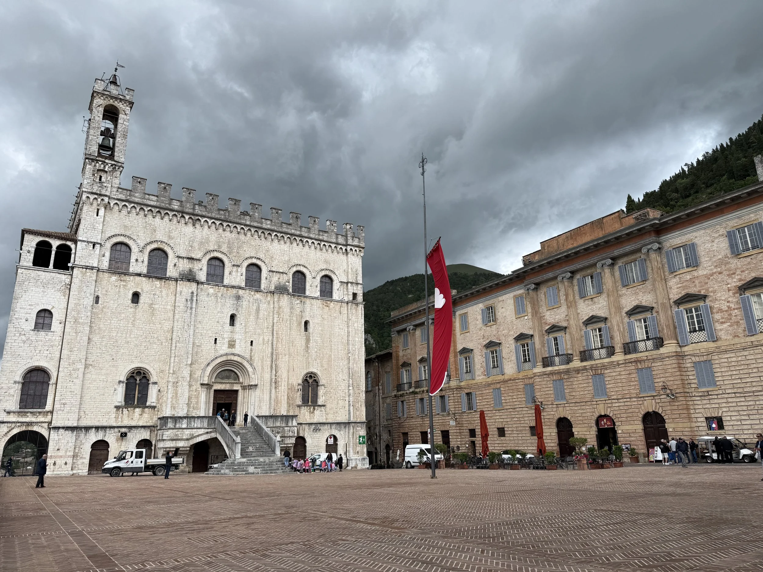 Historic stone church with a tall bell tower, surrounded by a town square, cloudy sky, and people walking.