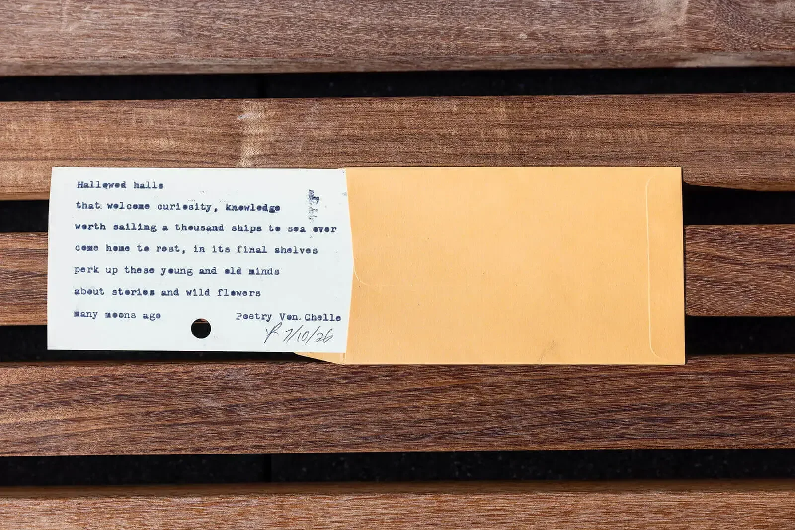 A poem printed on a white and yellow card with a hole punch at the bottom left corner, placed on a wooden surface.