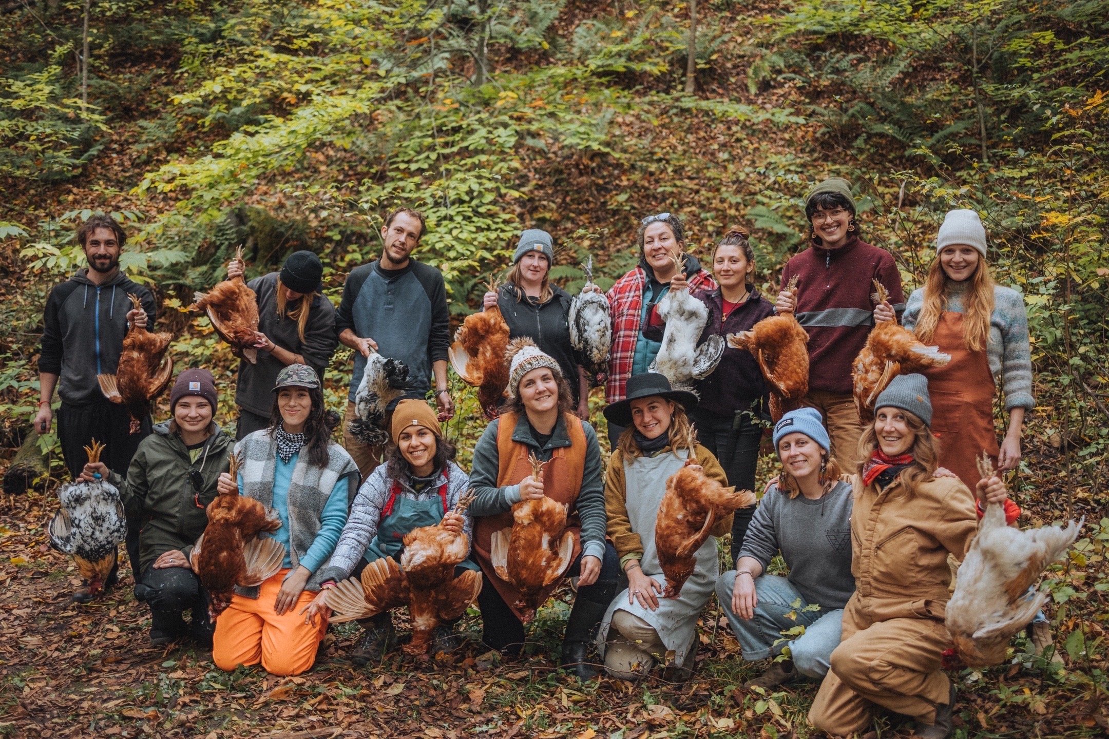 Group of people holding chickens in a wooded area.