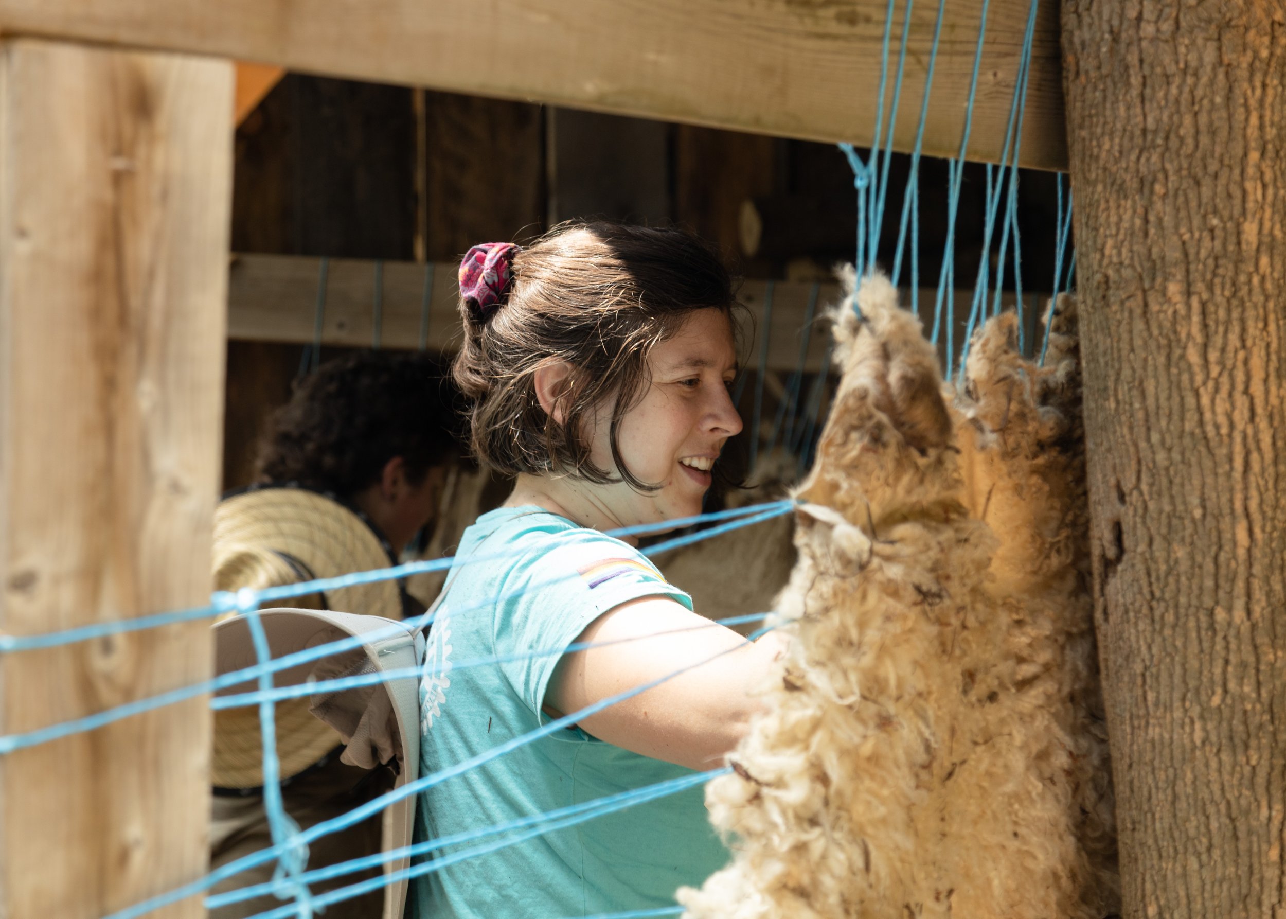 Person working with wool hanging on blue strings outdoors.