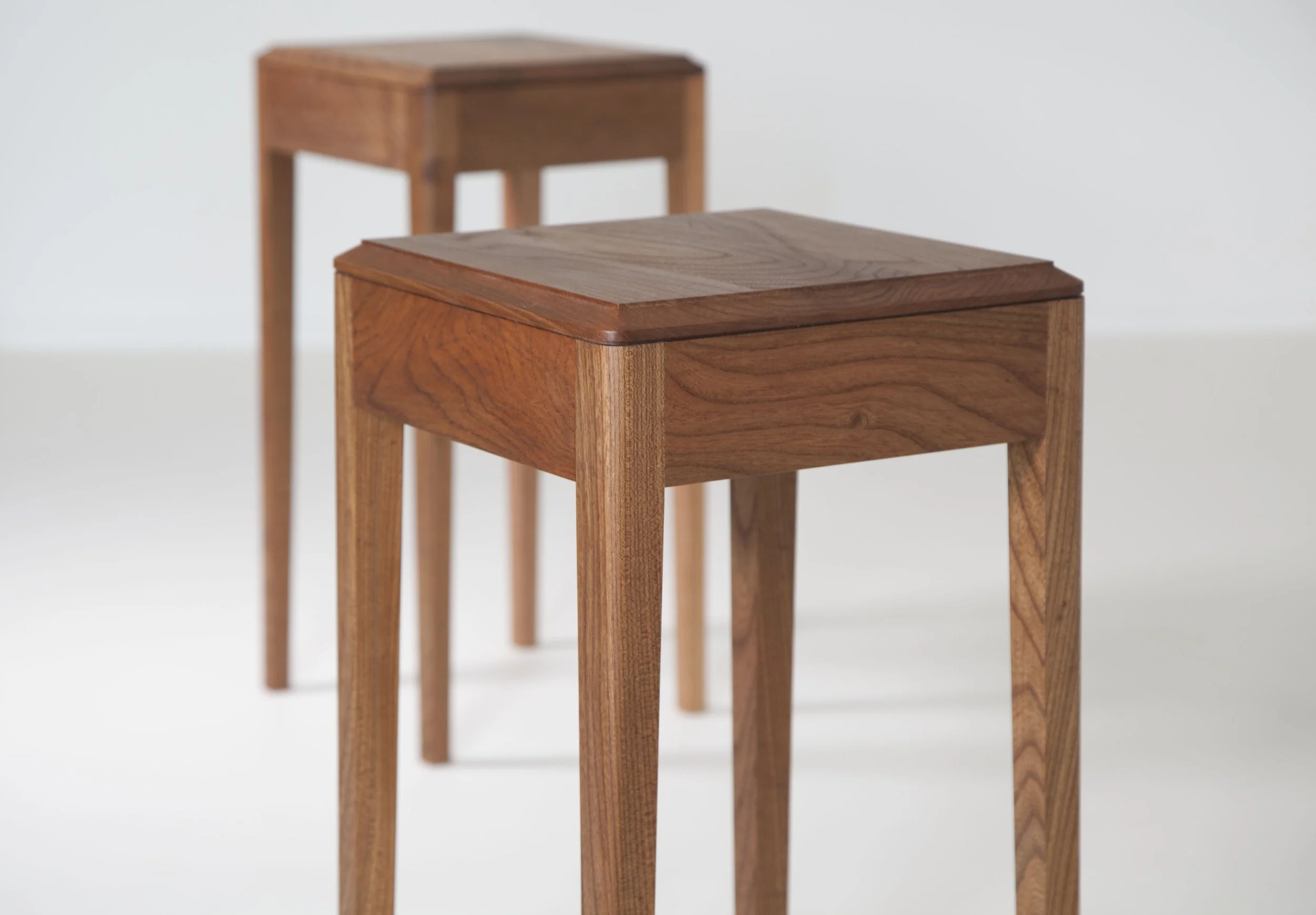 Two wooden nesting tables of different sizes with squared tabletops and four tapering legs, placed against a white background.