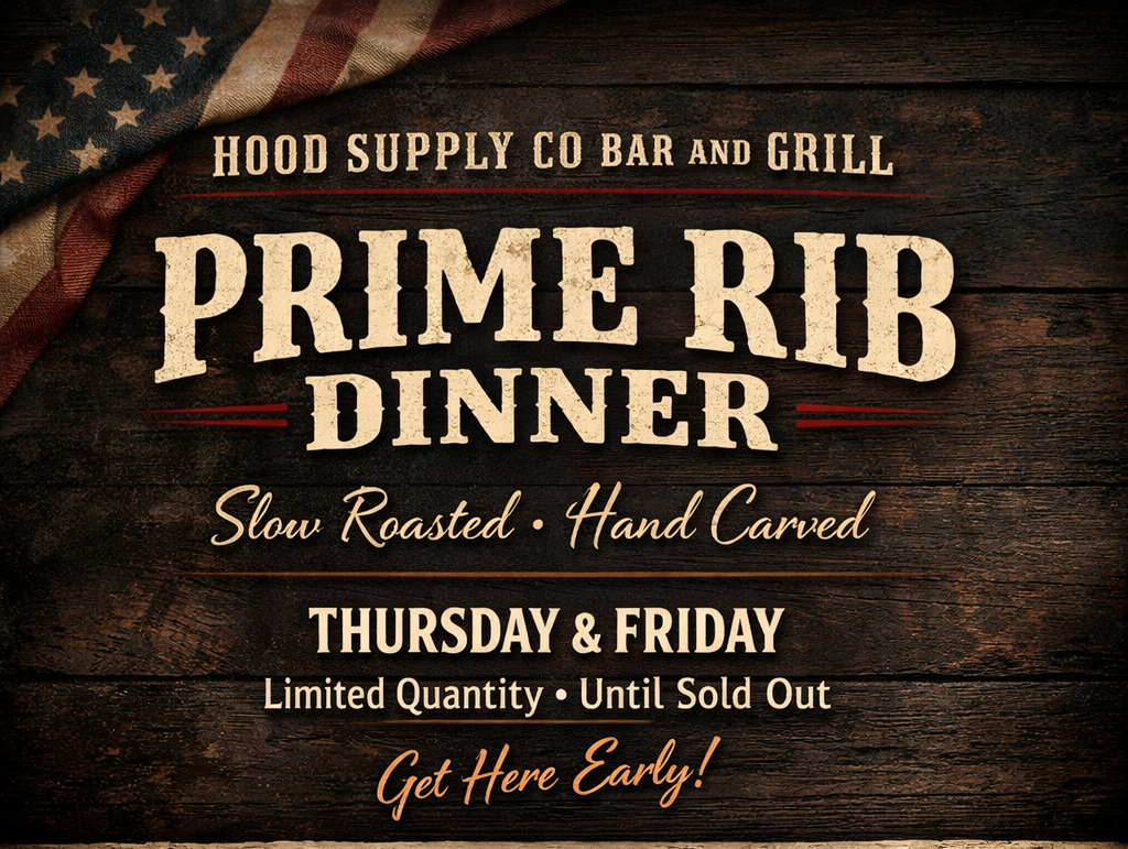 A sign advertising prime rib dinner at Hood Supply Co Bar and Grill, offering slow roasted, hand carved prime rib on Thursday and Friday, with limited quantity until sold out, encouraging customers to get there early. The background features dark wood and a part of an American flag in the upper left corner.