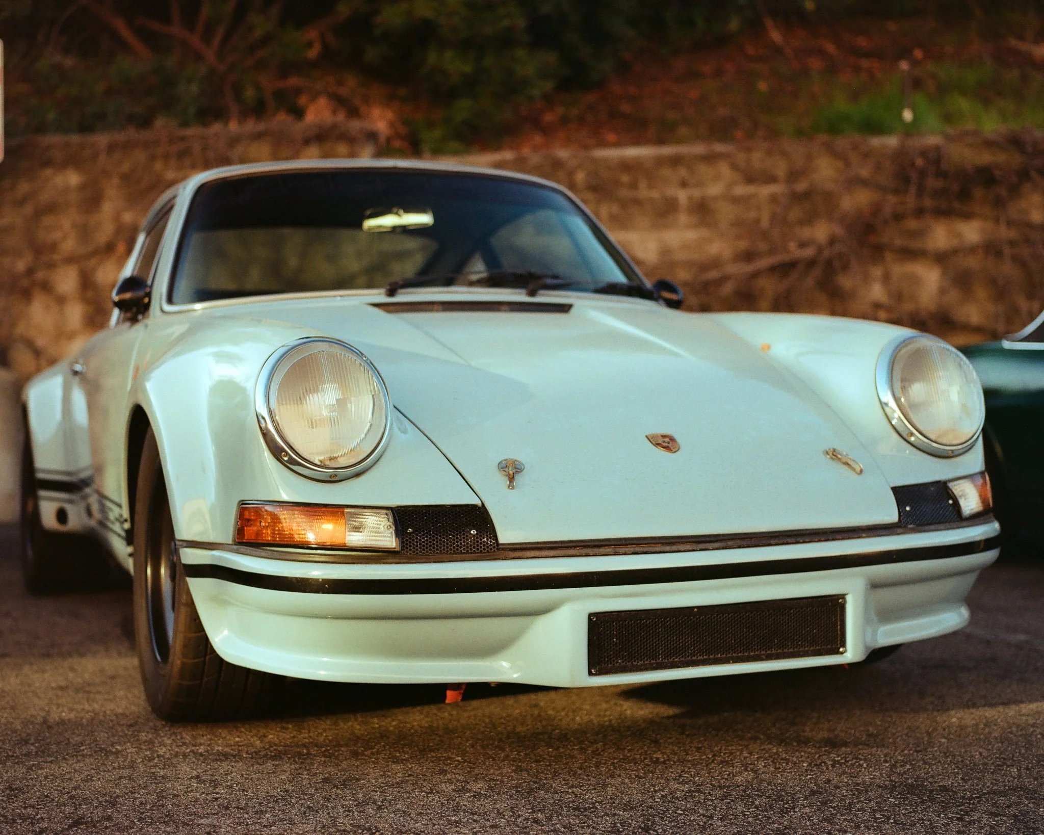 A vintage white Porsche 911 sports car parked outdoors at sunset.