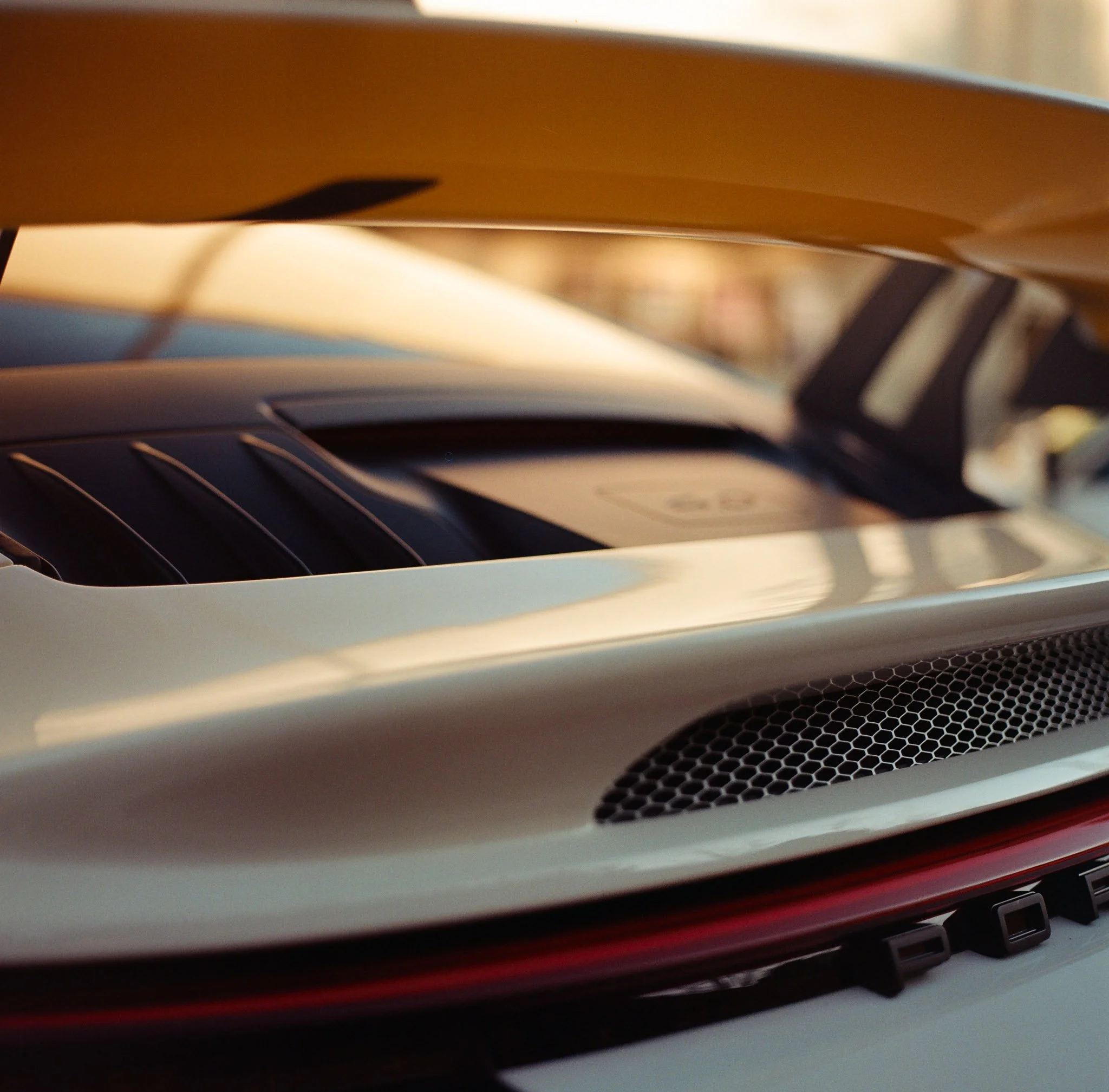 Close-up of a white sports car's rear engine vent with a blurred background.
