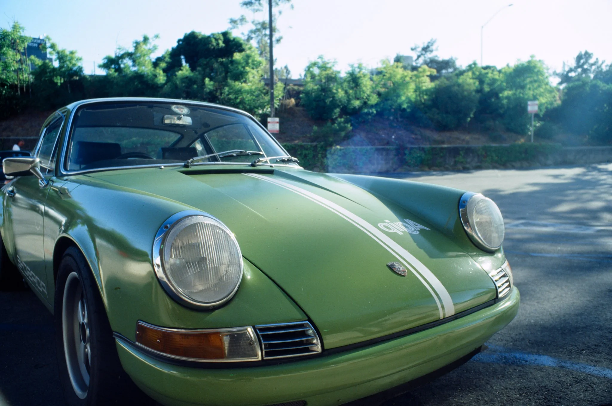 A green vintage Porsche 911 with white racing stripes parked outdoors on a sunny day.