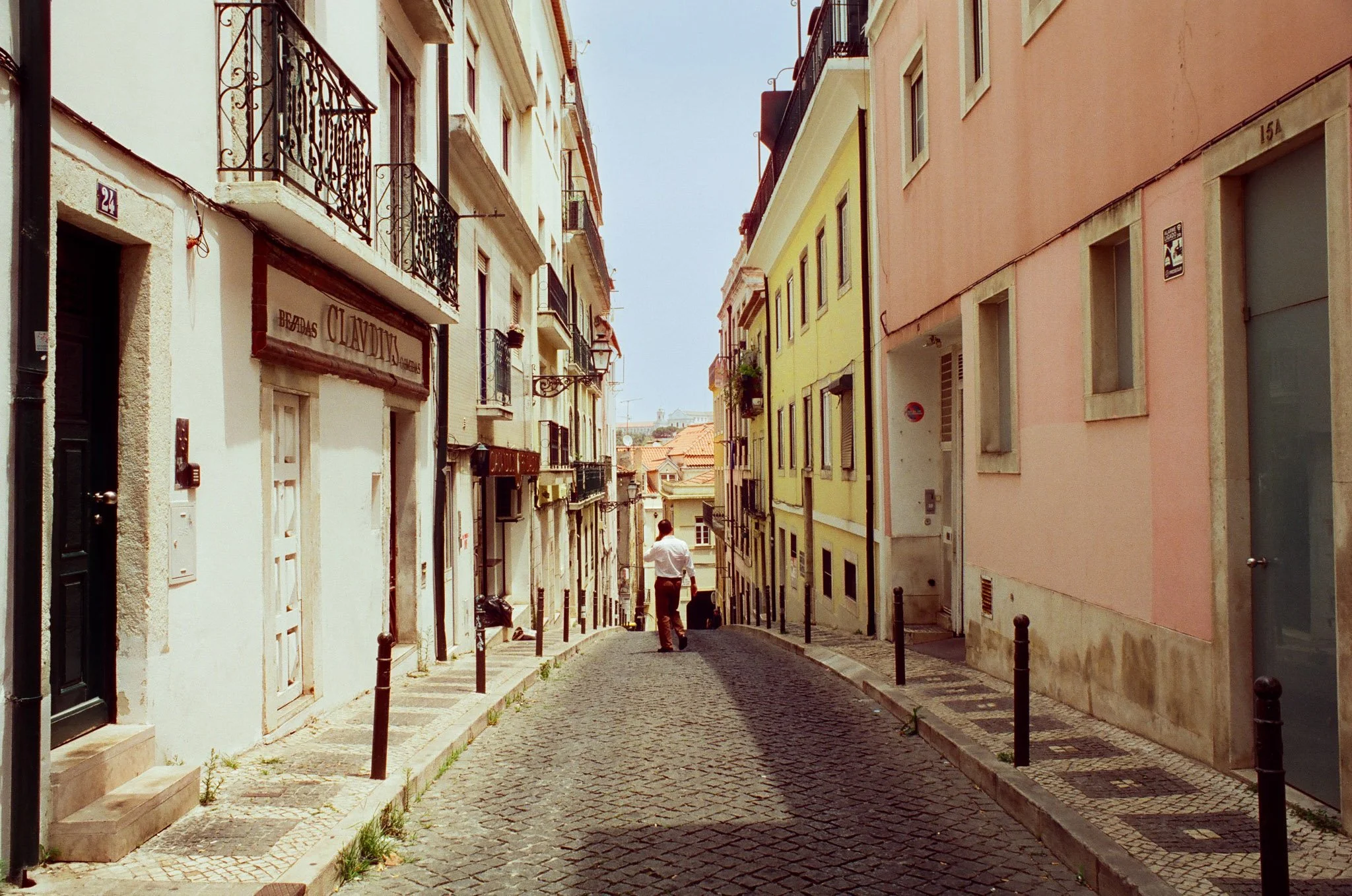 A narrow cobblestone street lined with colorful European-style buildings, with one man walking away from the camera.