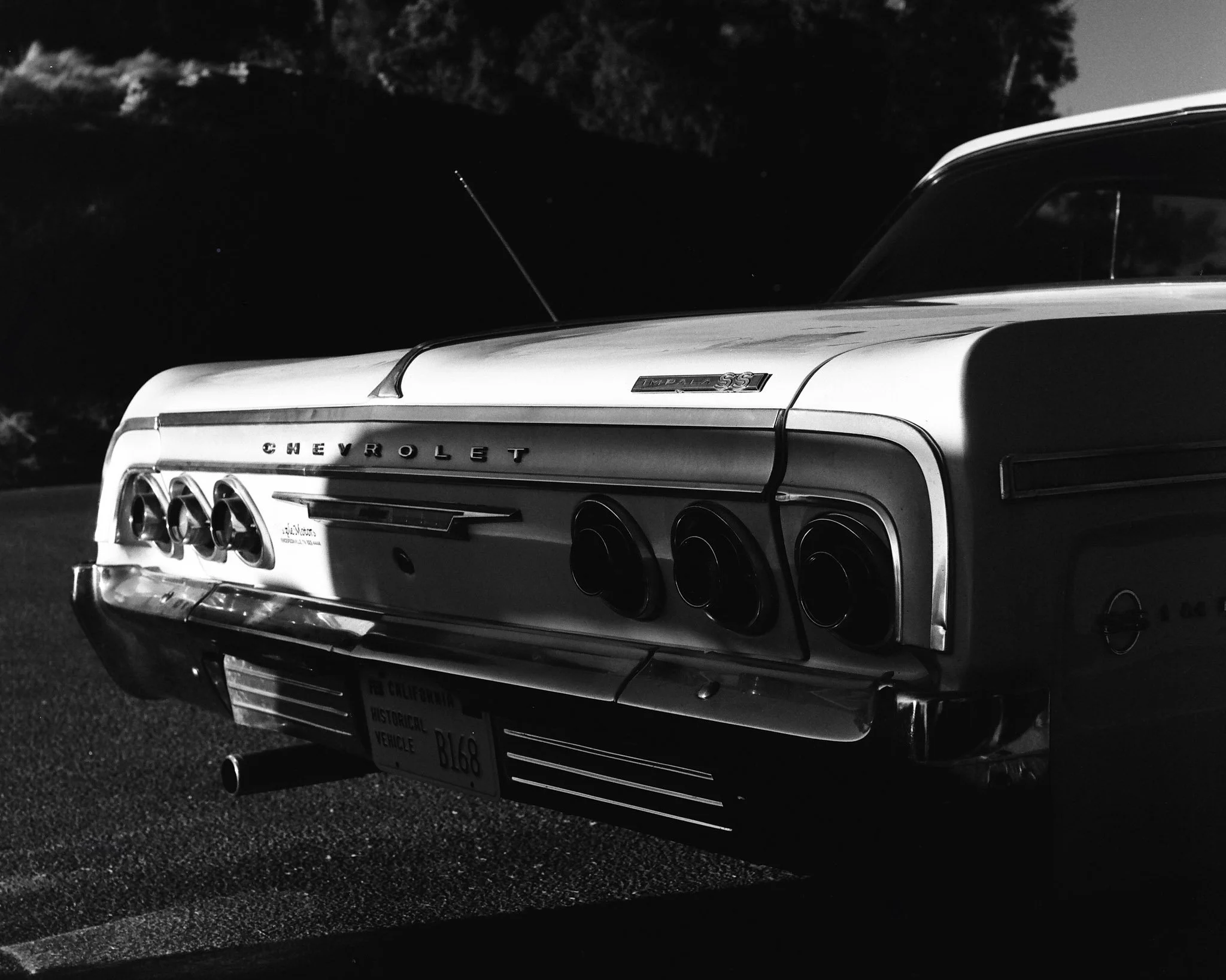 Rear view of a vintage Chevrolet Impala SS car in black and white, showing taillights, bumper, and license plate, parked outdoors at night.