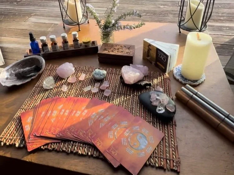 Tarot cards on mat with crystals, essential oils, a candle, and a book on a wooden table.