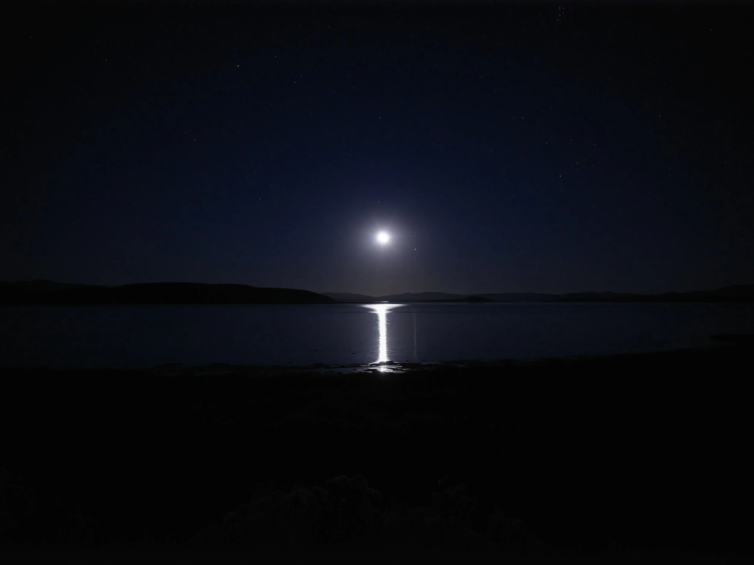 Night scene with a bright moon reflecting on a calm body of water, surrounded by dark hills and a starry sky.
