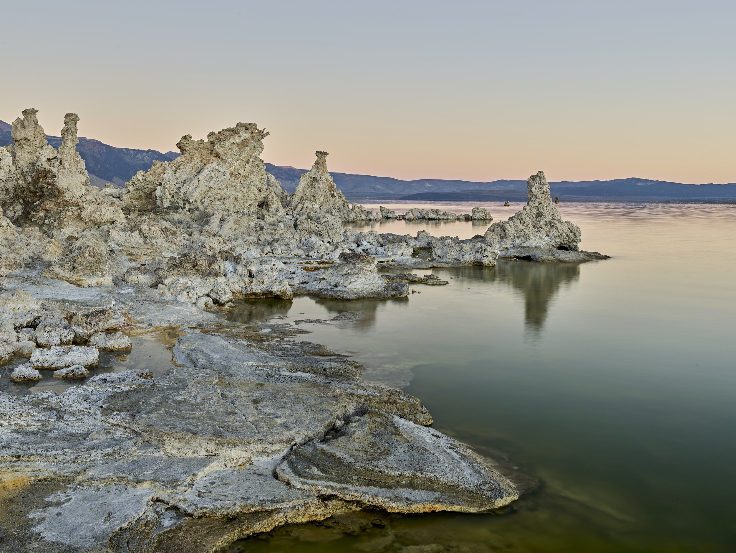 Calcium deposits forming unique rock formations along the shoreline of a lake during sunset, with mountains in the background.