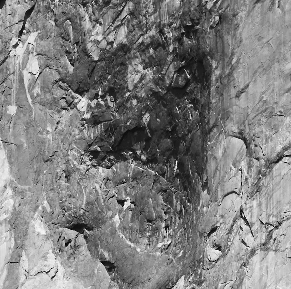 Black and white photograph of a rugged, cracked rock face or cliff.