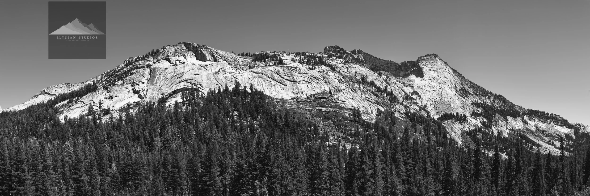 Black and white photograph of a mountain range with rocky peaks and a dense forest at the base