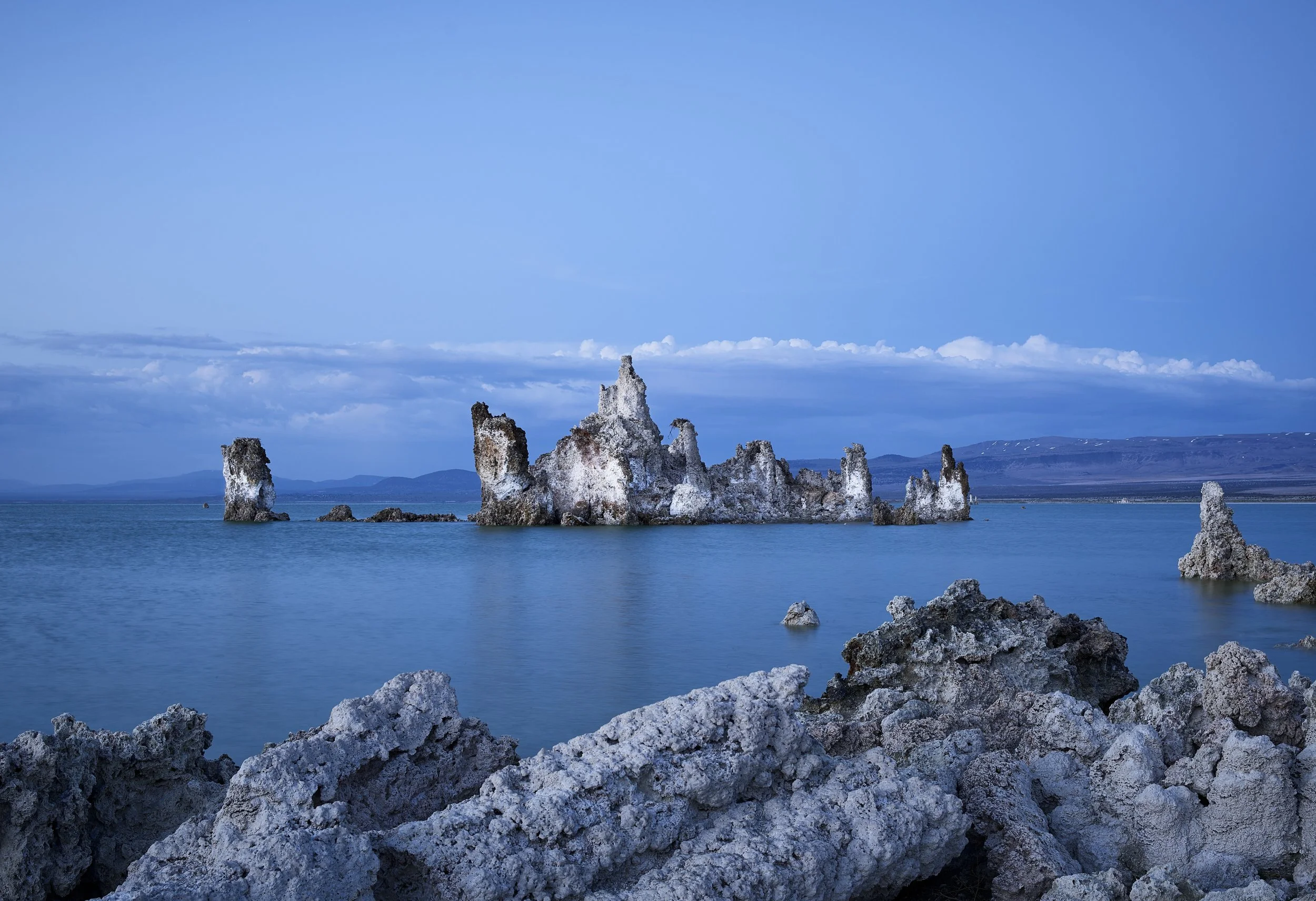 Rock formations in a blue aquatic landscape with distant mountains and a partly cloudy sky.