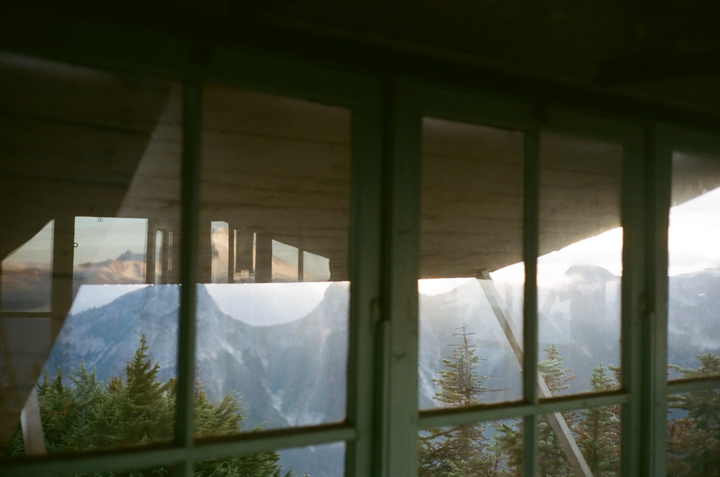 View of mountains and trees through a window with multiple panes, with a building's ceiling and part of the wall visible in the foreground.