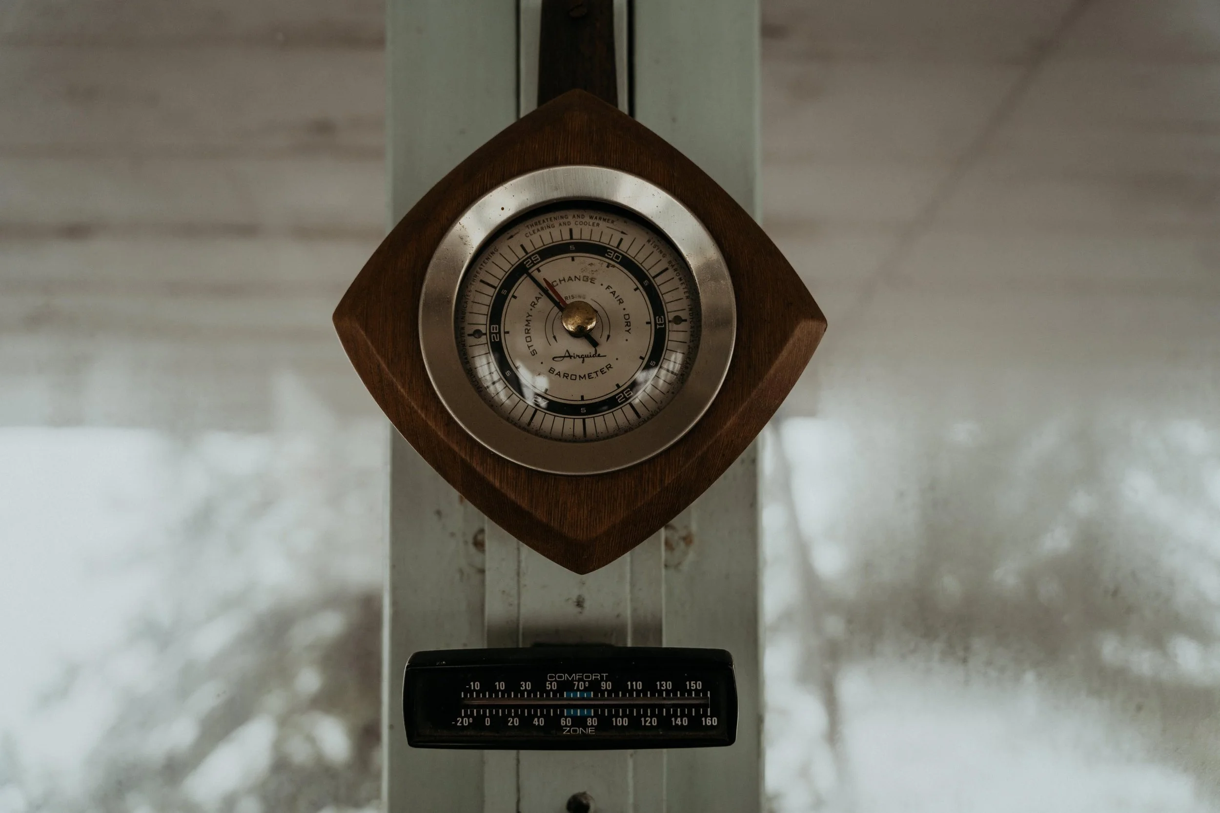 A wooden framed barometric weather station with an analog dial indicating pressure and a black comfort zone thermometer below it.