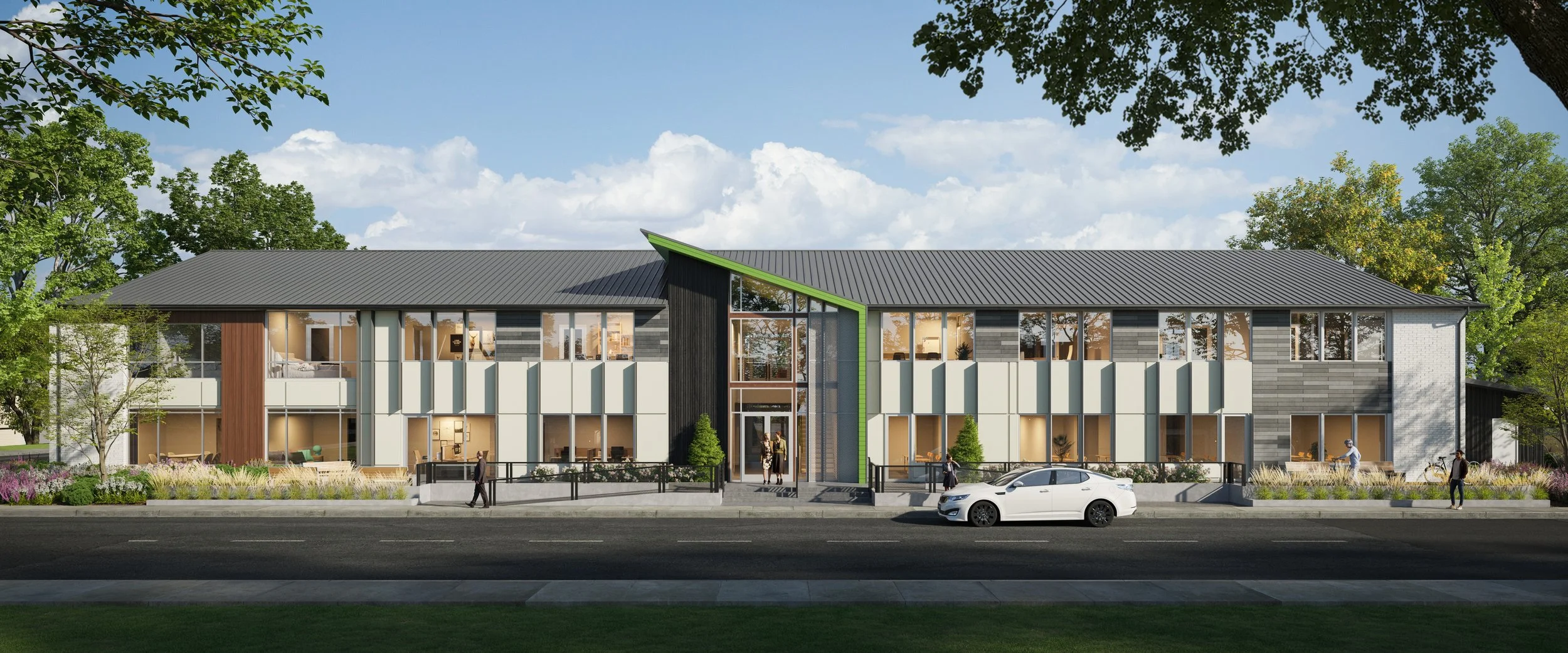 A modern community area with a wooden walkway, benches, and lush green trees. There are people sitting and walking, with contemporary townhouses featuring green roofs in the background. The scene is bright with a blue sky and a sunny atmosphere.