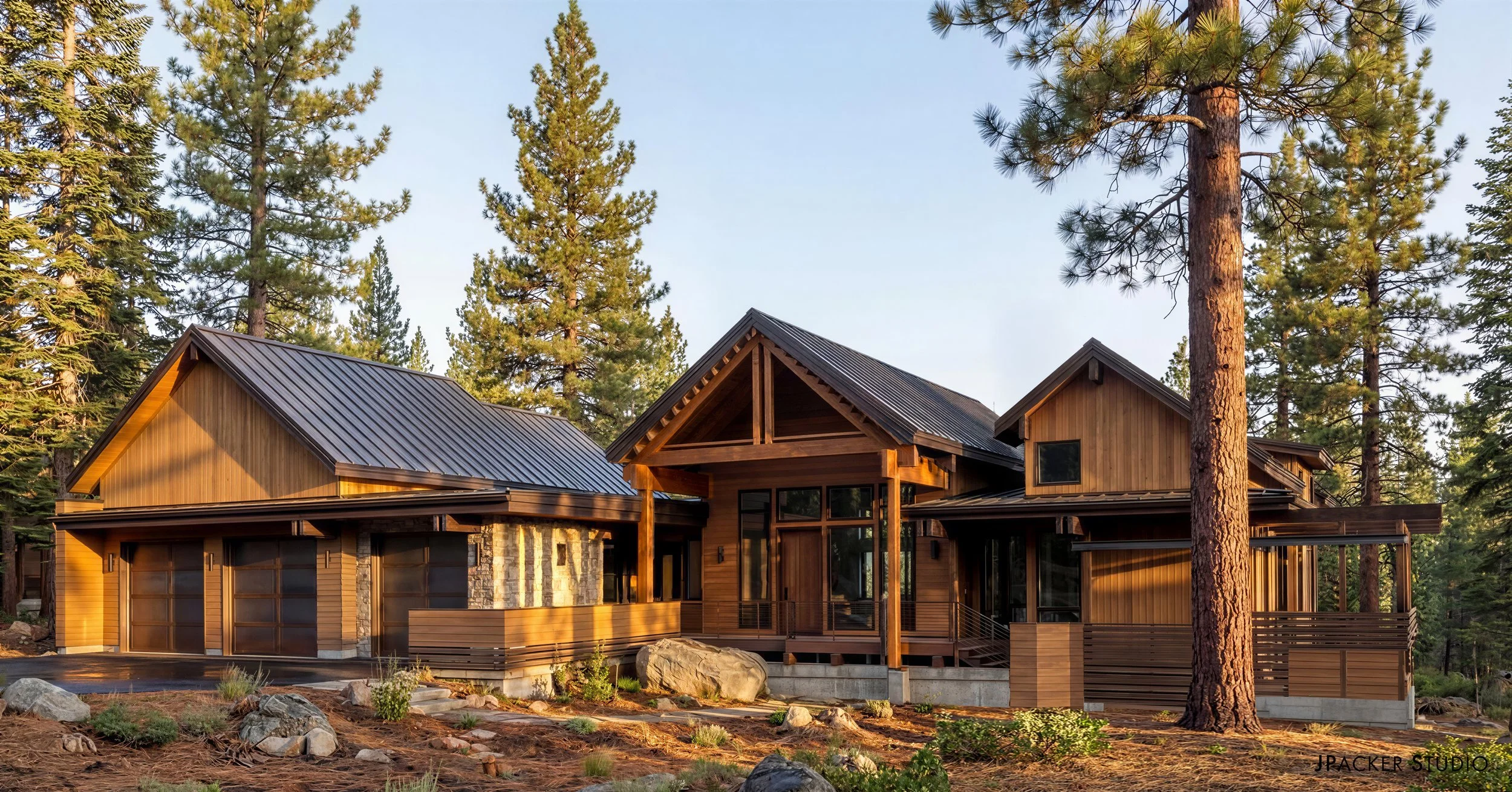 A modern house with wooden and stone exterior walls, large windows, and a metal roof, situated among tall pine trees in a forested area.
