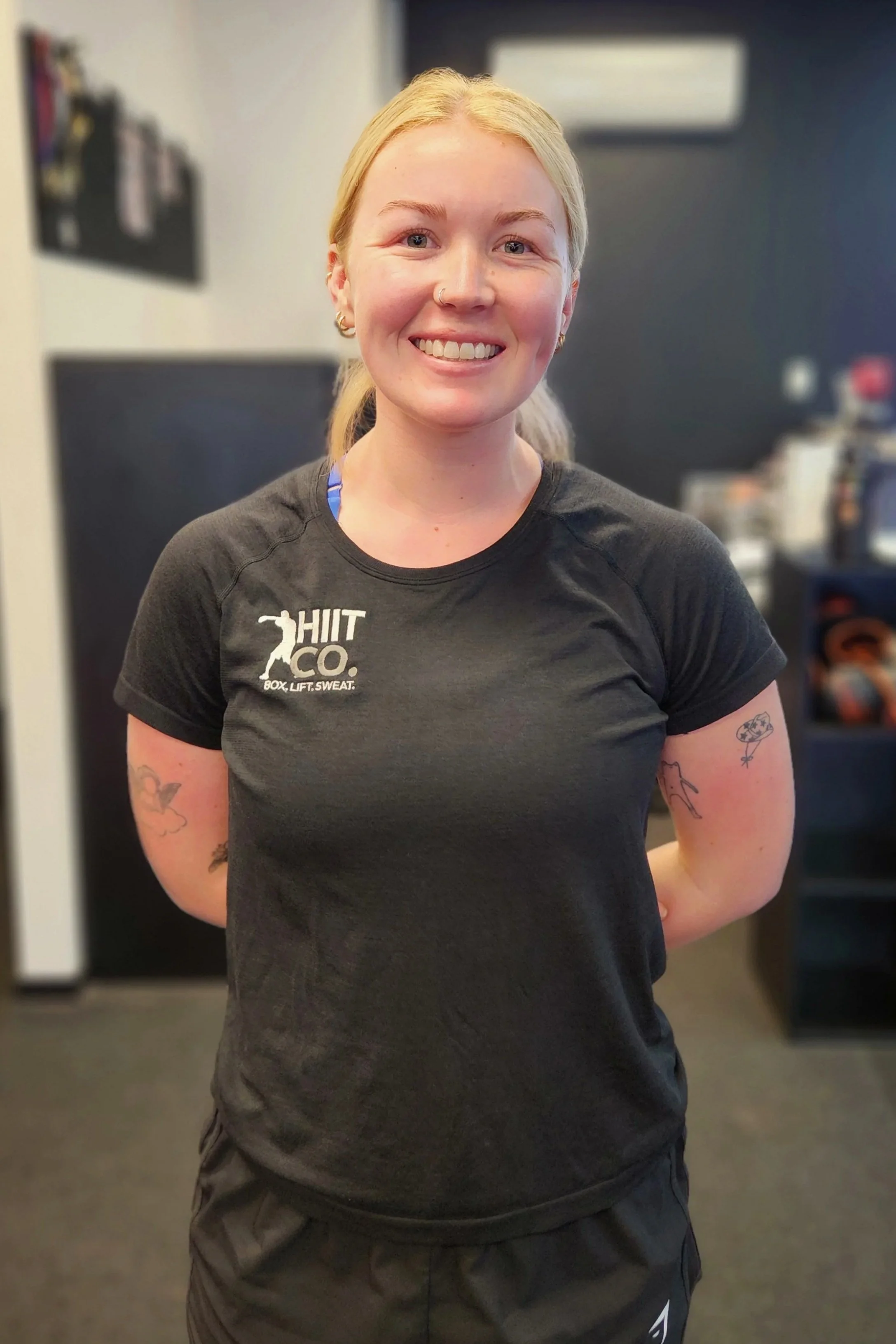 A smiling woman with natural curly hair, glasses, earrings, and layered necklaces.