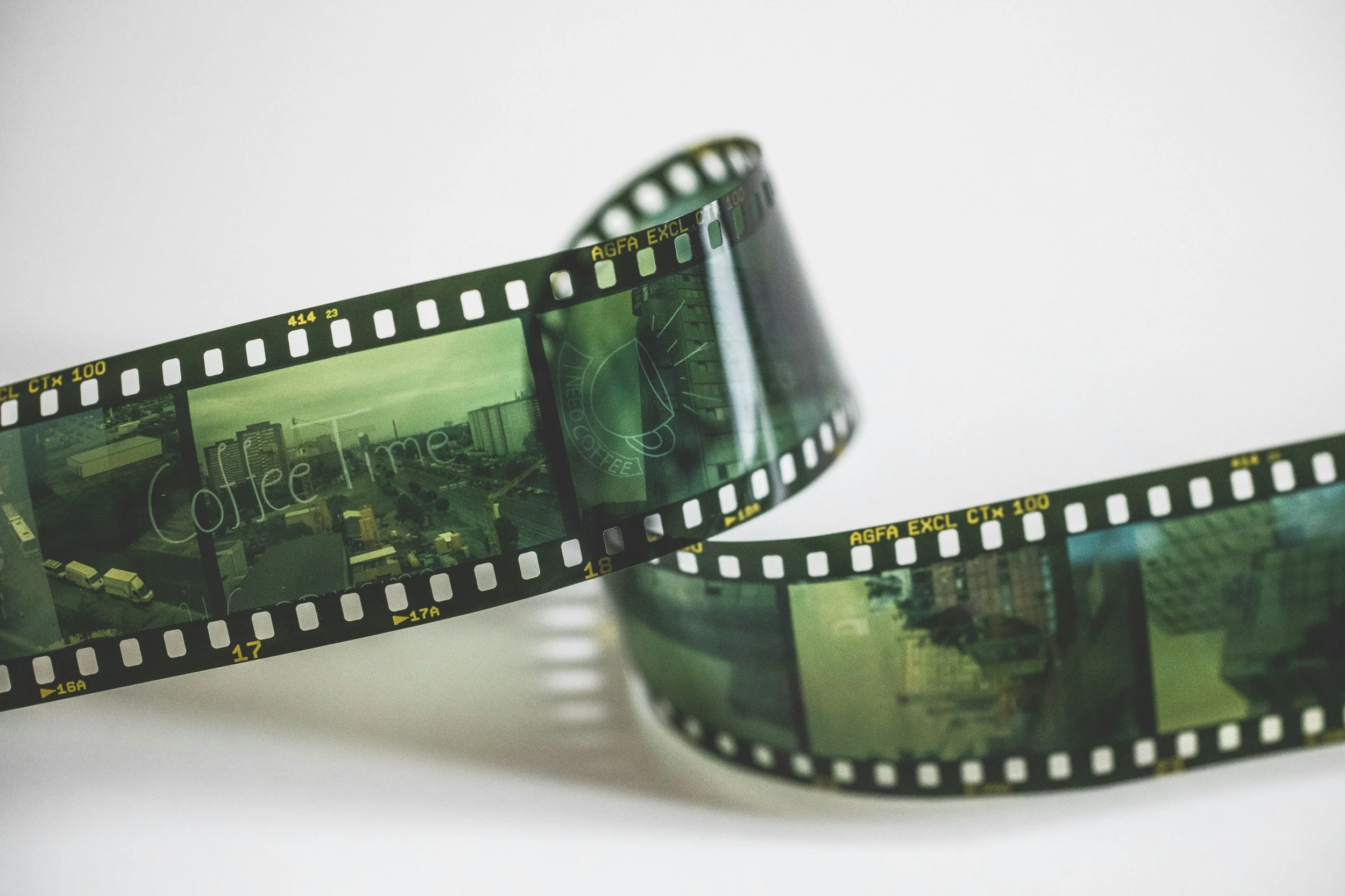 A reel of photographic film, partially unrolled, with images visible along the strip, placed in a plastic container.