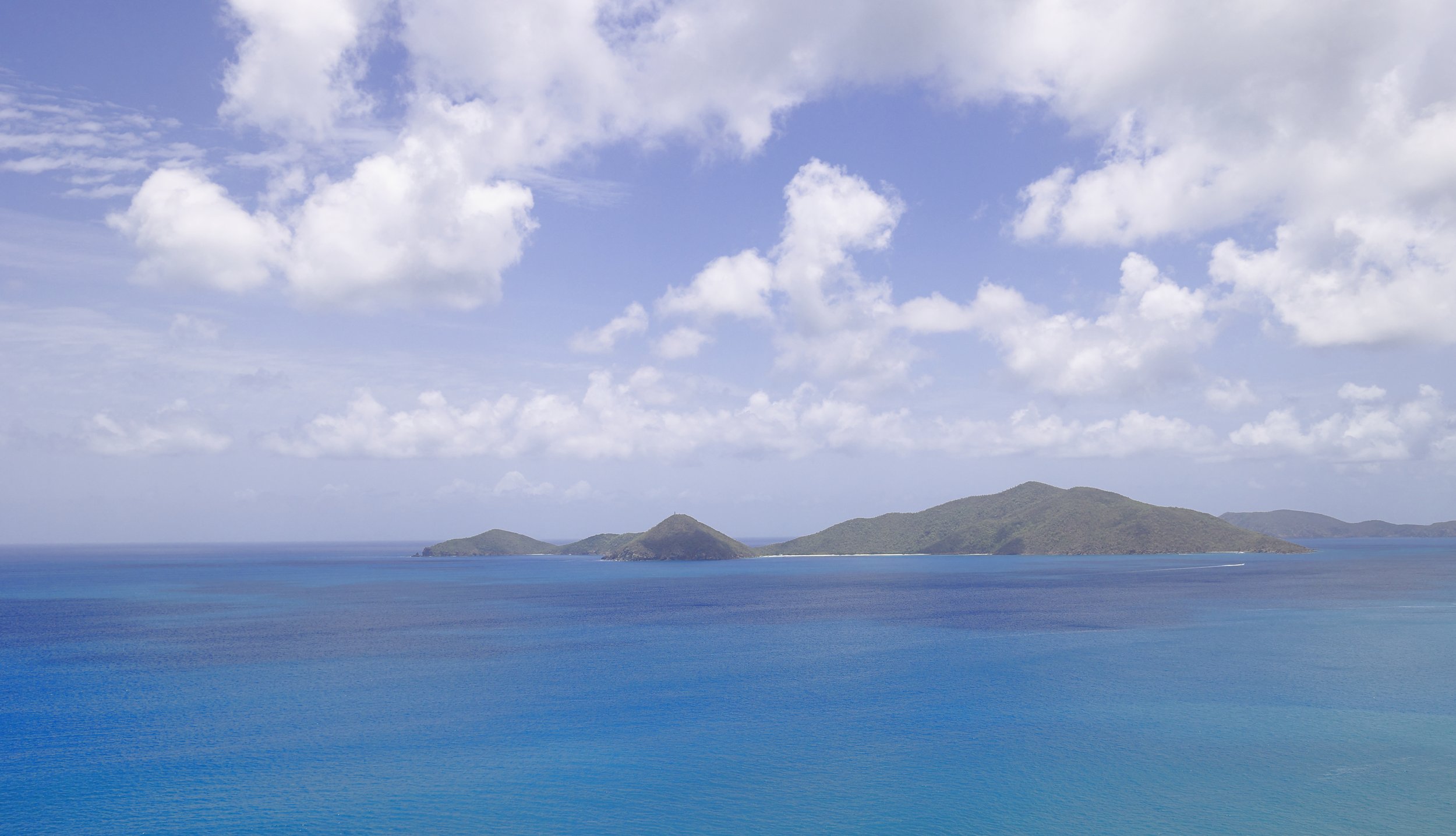 A scenic view of the ocean with blue water and small islands in the distance under a partly cloudy sky.