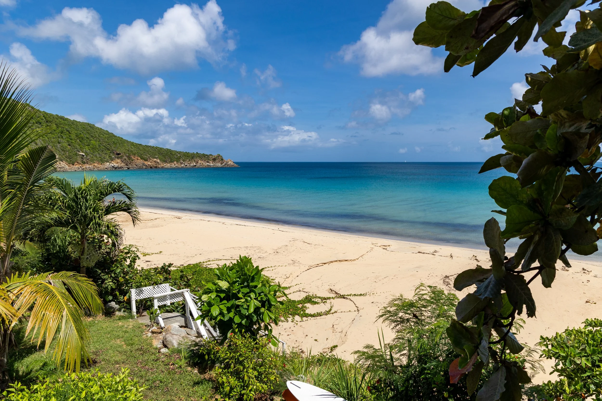 A serene beach named lambert beach in the virgin islands with white sand, turquoise water, and lush green vegetation under a blue sky with scattered clouds.