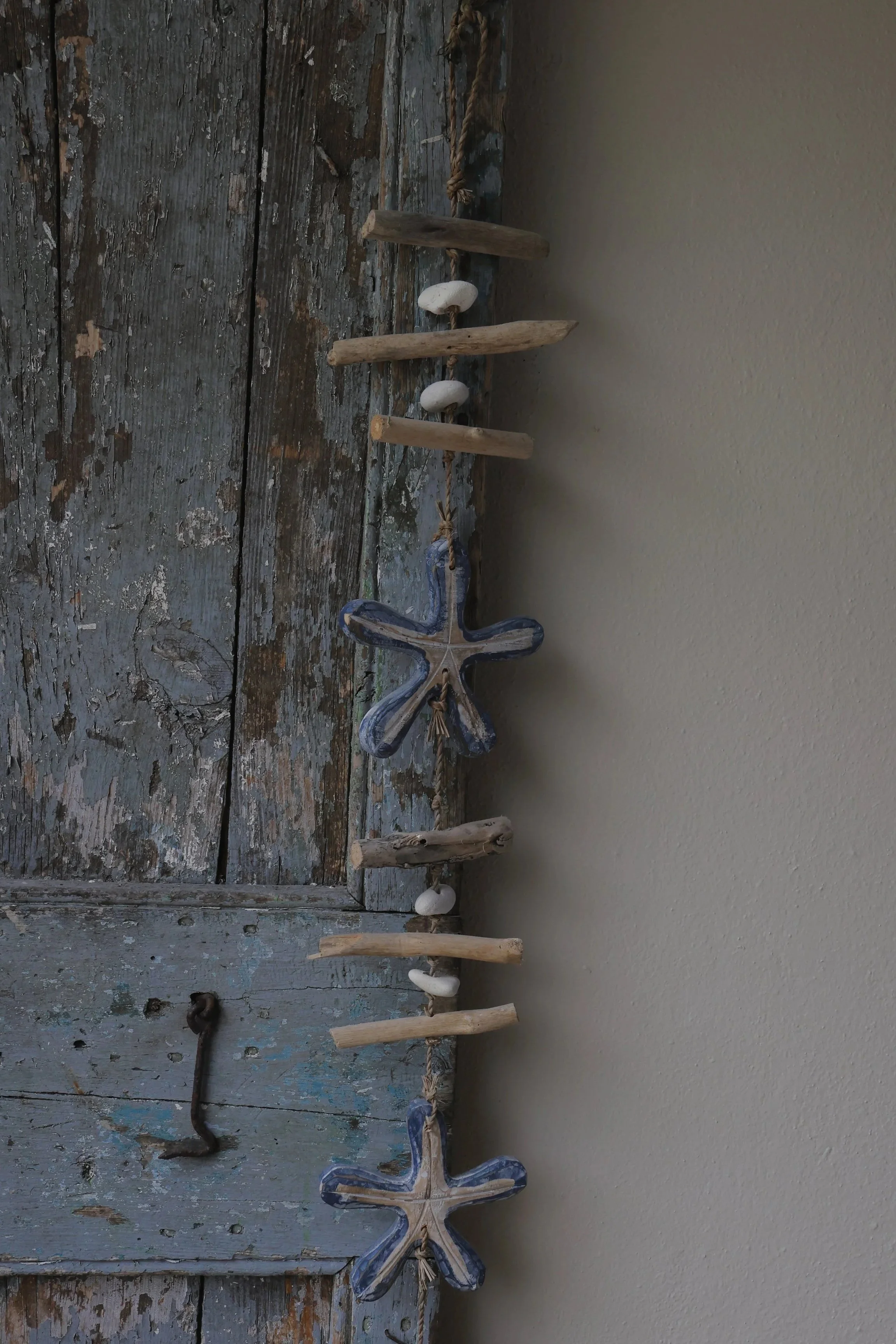 Decorative wall hanging made of driftwood, seashells, and ceramic starfish, mounted on a rustic wooden door.