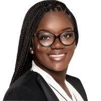 A smiling woman with glasses and braids, wearing a black blazer and white shirt.