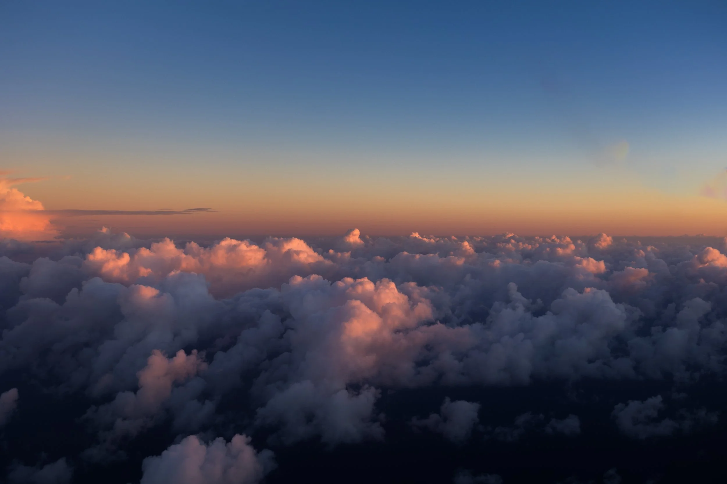 A view of colorful clouds at sunset from above the clouds, with a clear sky overhead.