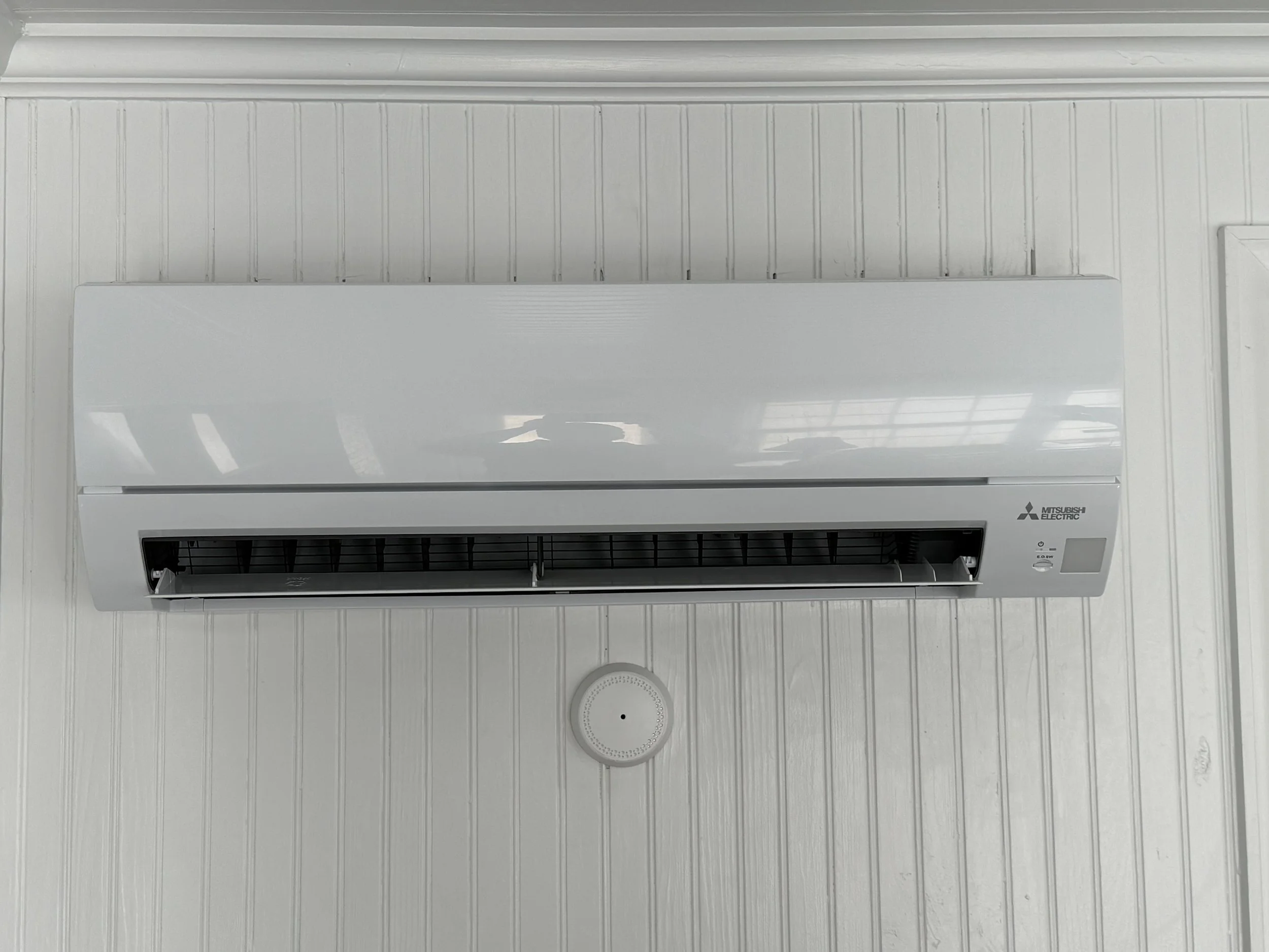 White Mitsubishi Electric wall-mounted air conditioner unit on a white paneled wall.