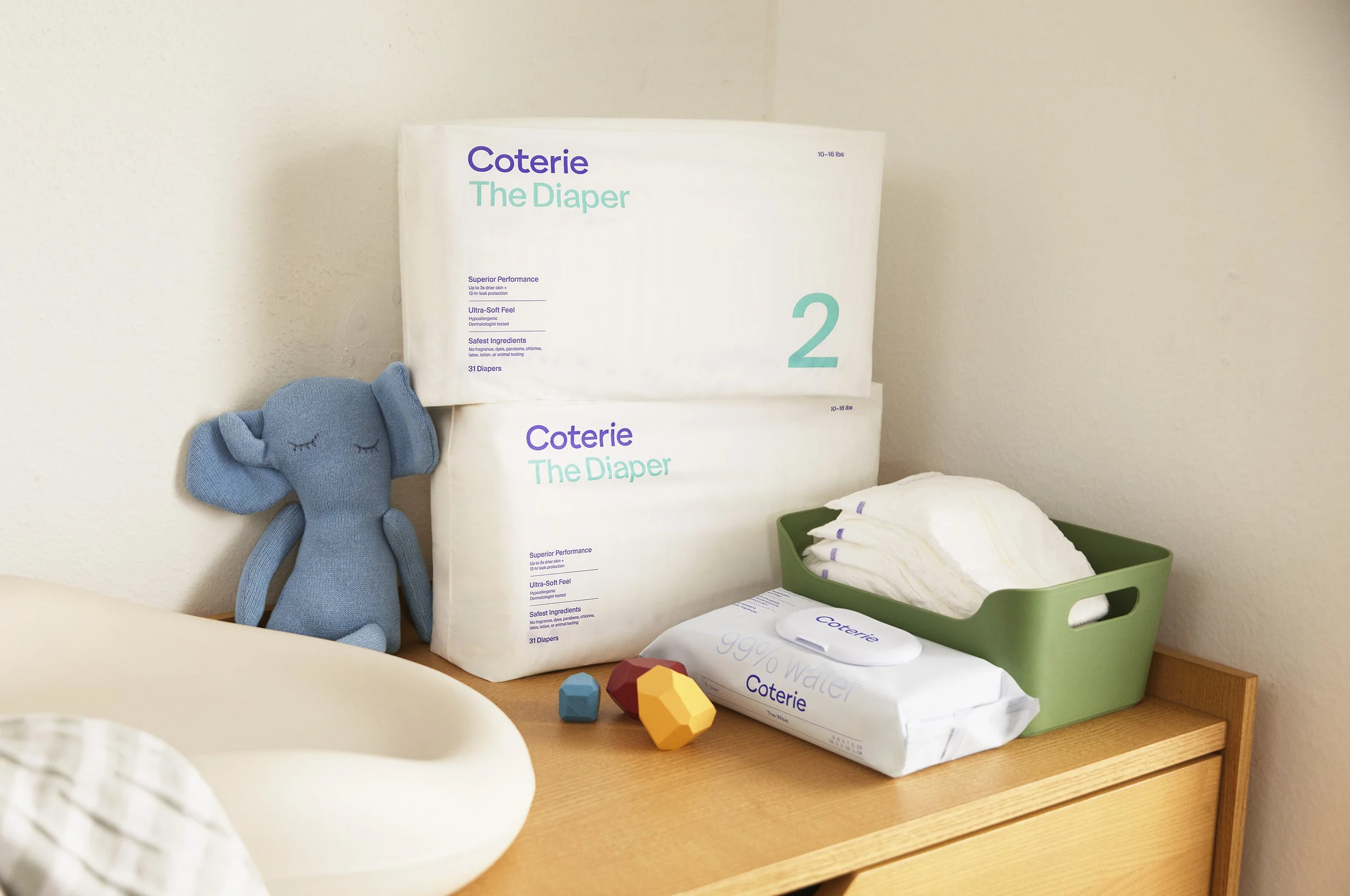 Coterie non-toxic diaper boxes and wipes styled on a nursery dresser next to a knit elephant toy