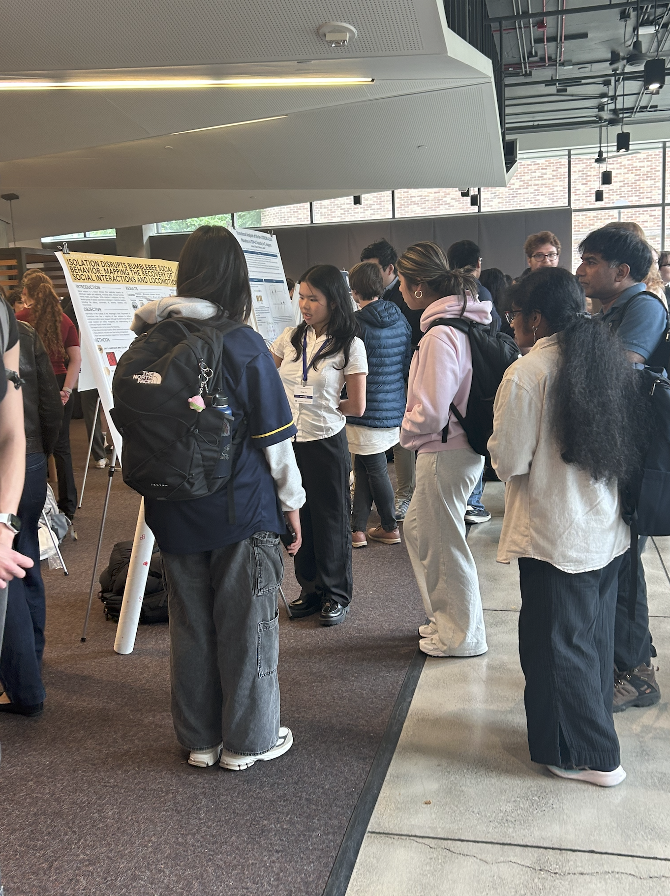 Elena stands in a white button-up and black dress pants presenting a research poster to an audience.