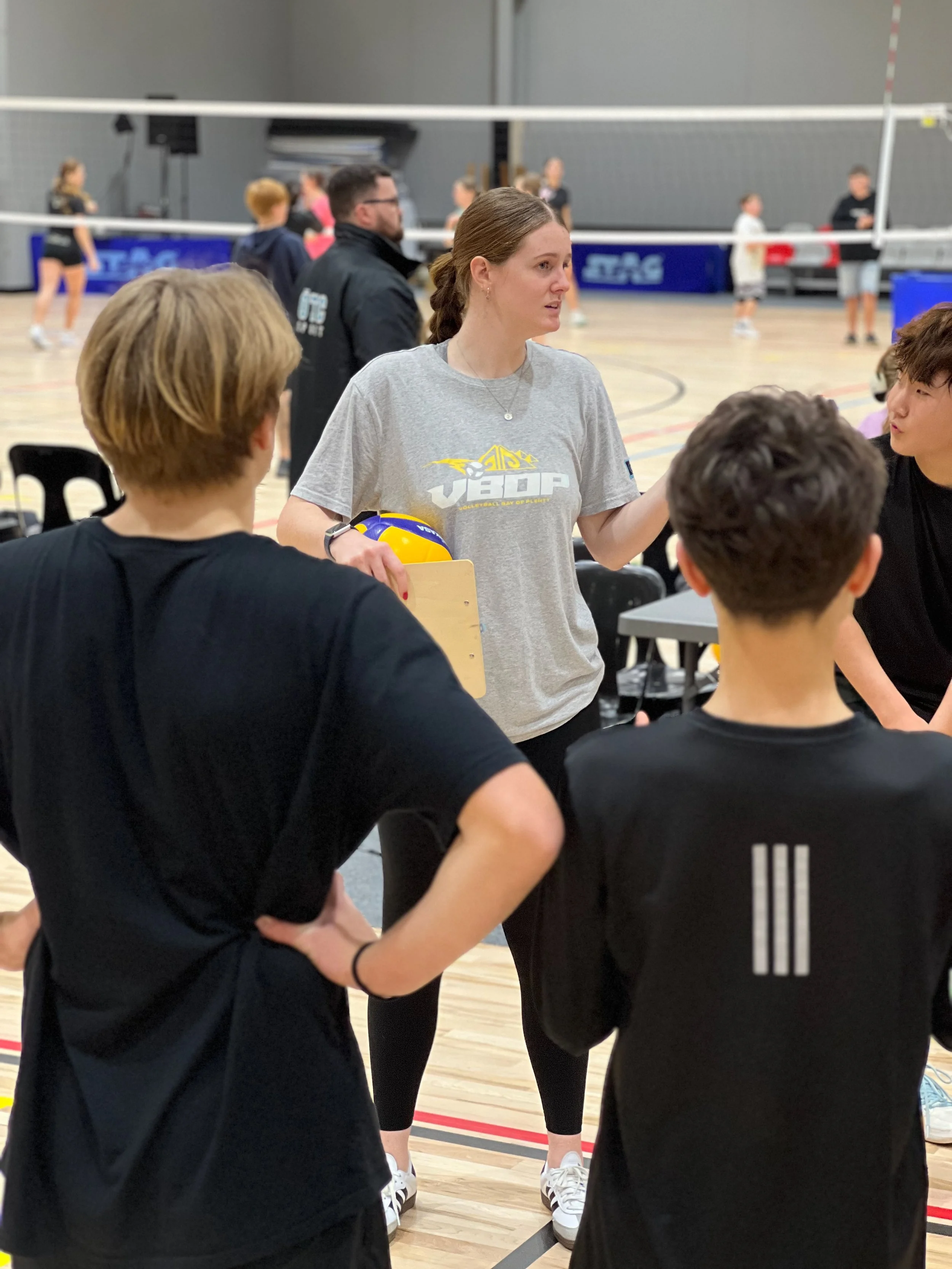 Girls volleyball coach giving instructions during practice in an indoor gymnasium.