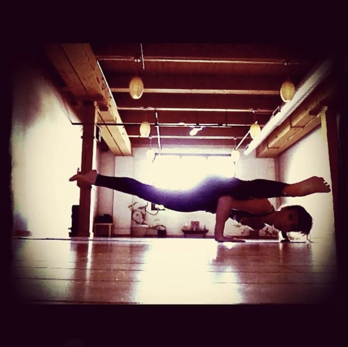 Person practicing a forearm balance yoga pose in a room with wooden ceiling and floors, natural light coming from a window at the back.