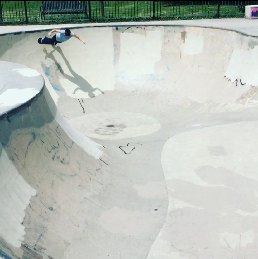 Skateboarder performing a trick in an empty concrete pool in a skatepark.