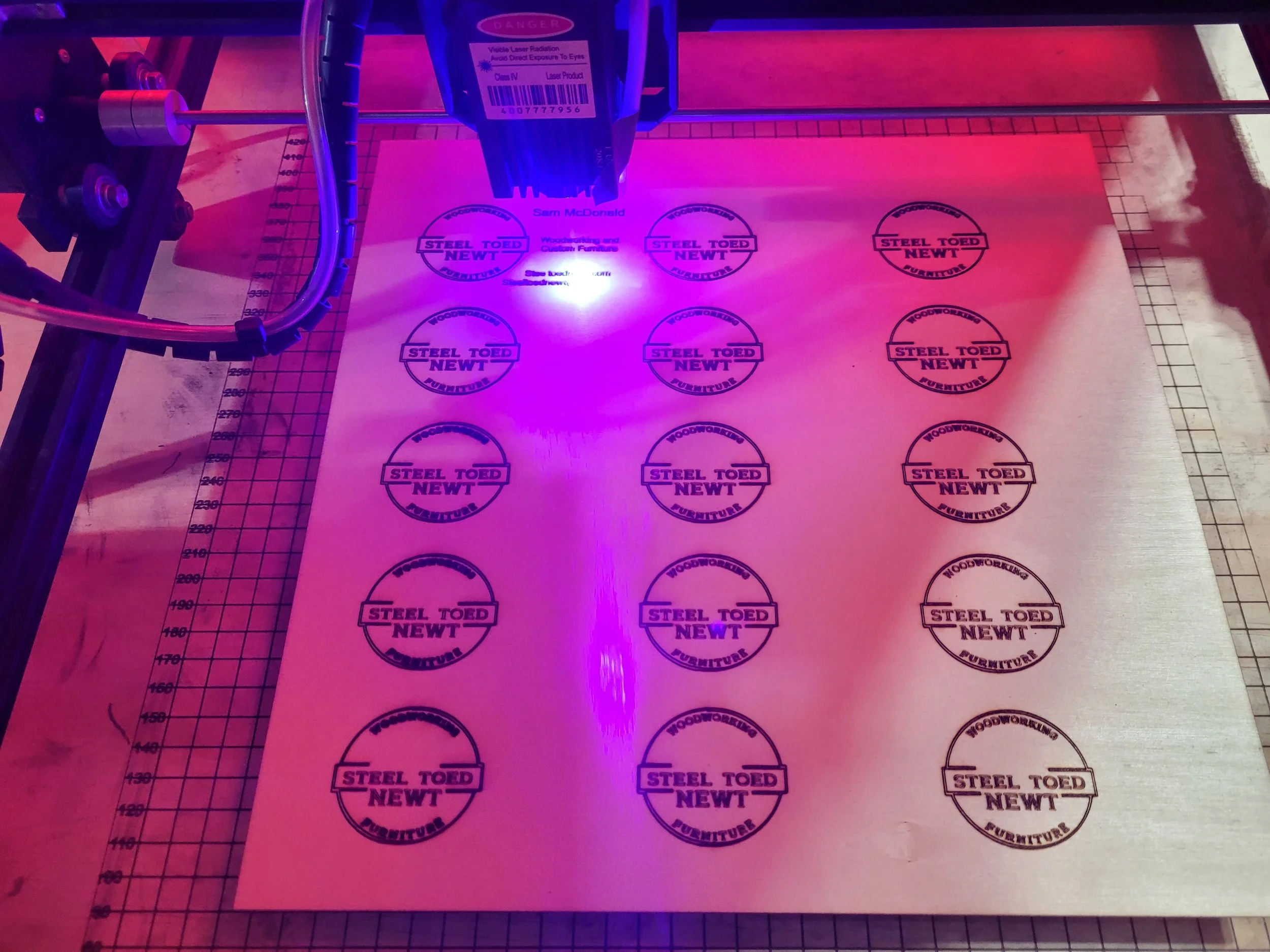 Full sheet of Steel Toed Newt circular logos being laser engraved on wood
