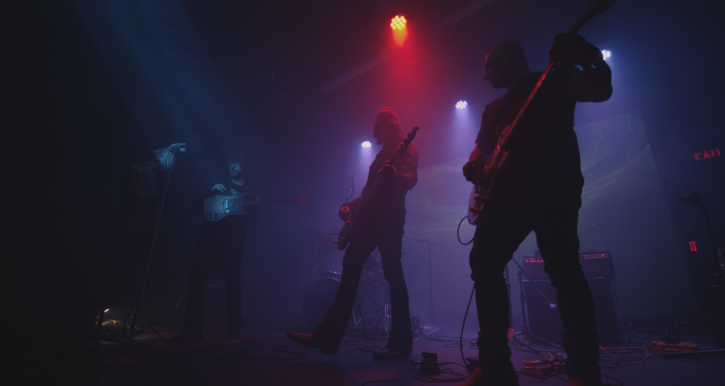 Silhouettes of three musicians playing electric guitars on stage with colorful lighting.