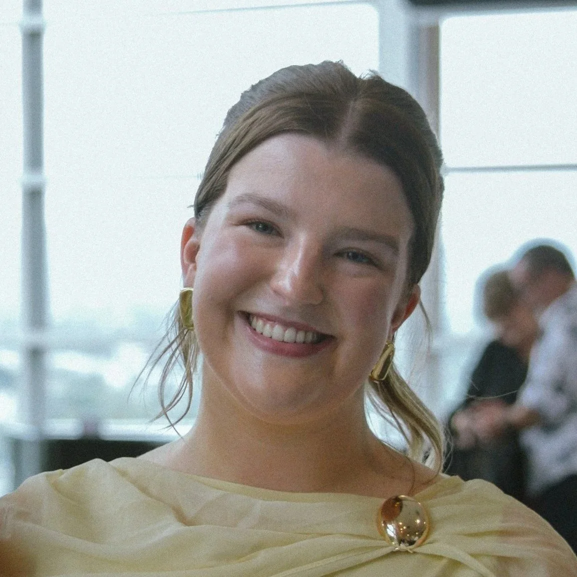 Smiling person with curly hair and glasses indoors