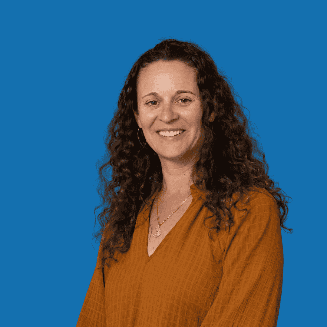 A woman with long curly hair wearing a brown blouse against a blue background.