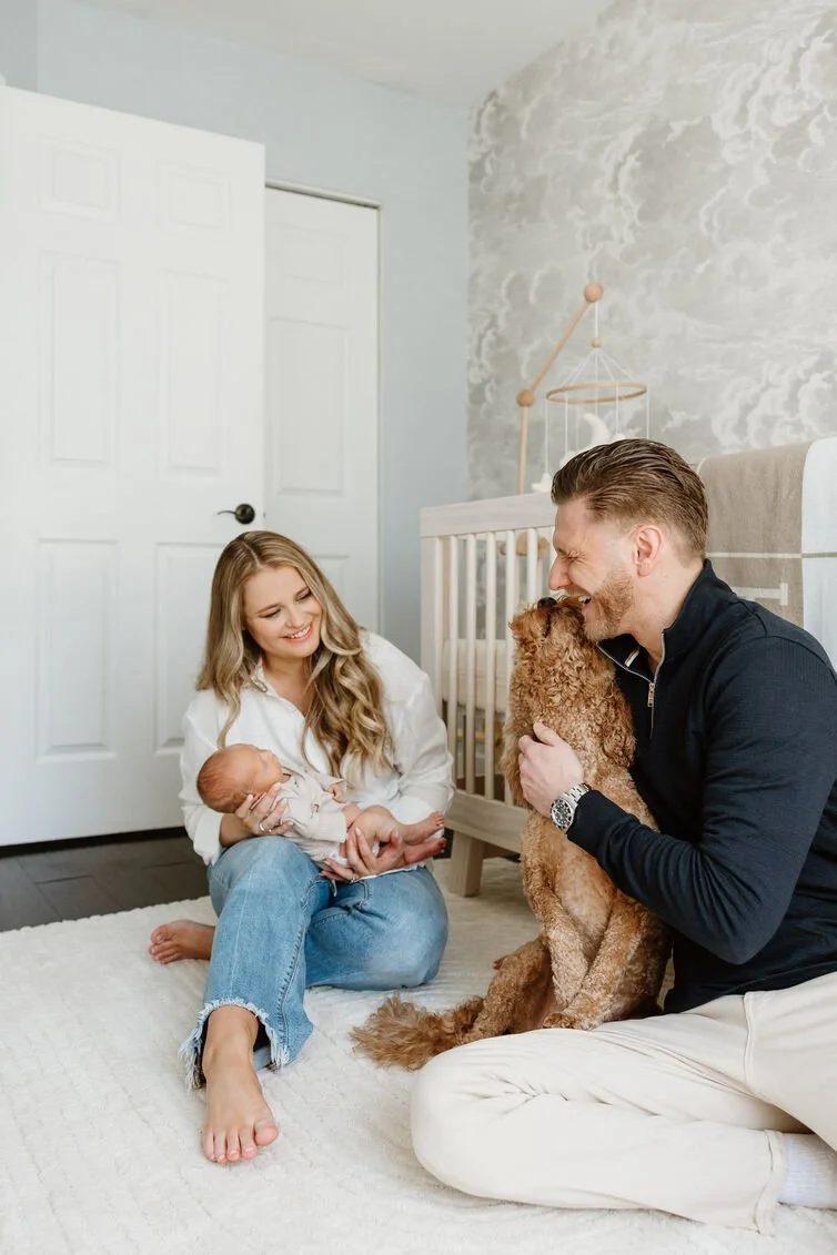 Family in nursery, woman holding newborn, man with dog, baby crib in background