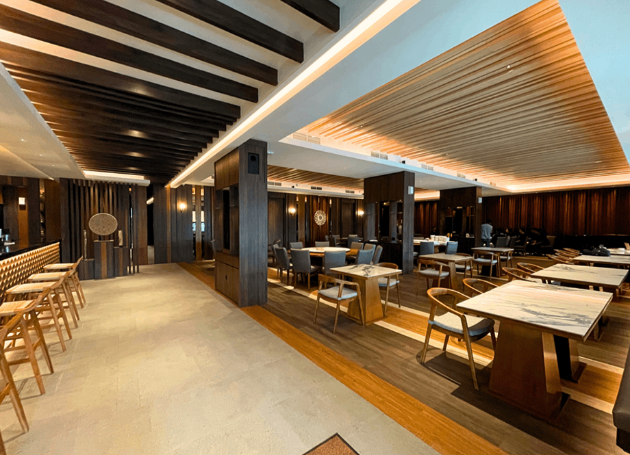 Interior of a modern restaurant or lounge with dark wood paneling, marble-topped tables, and upholstered chairs.