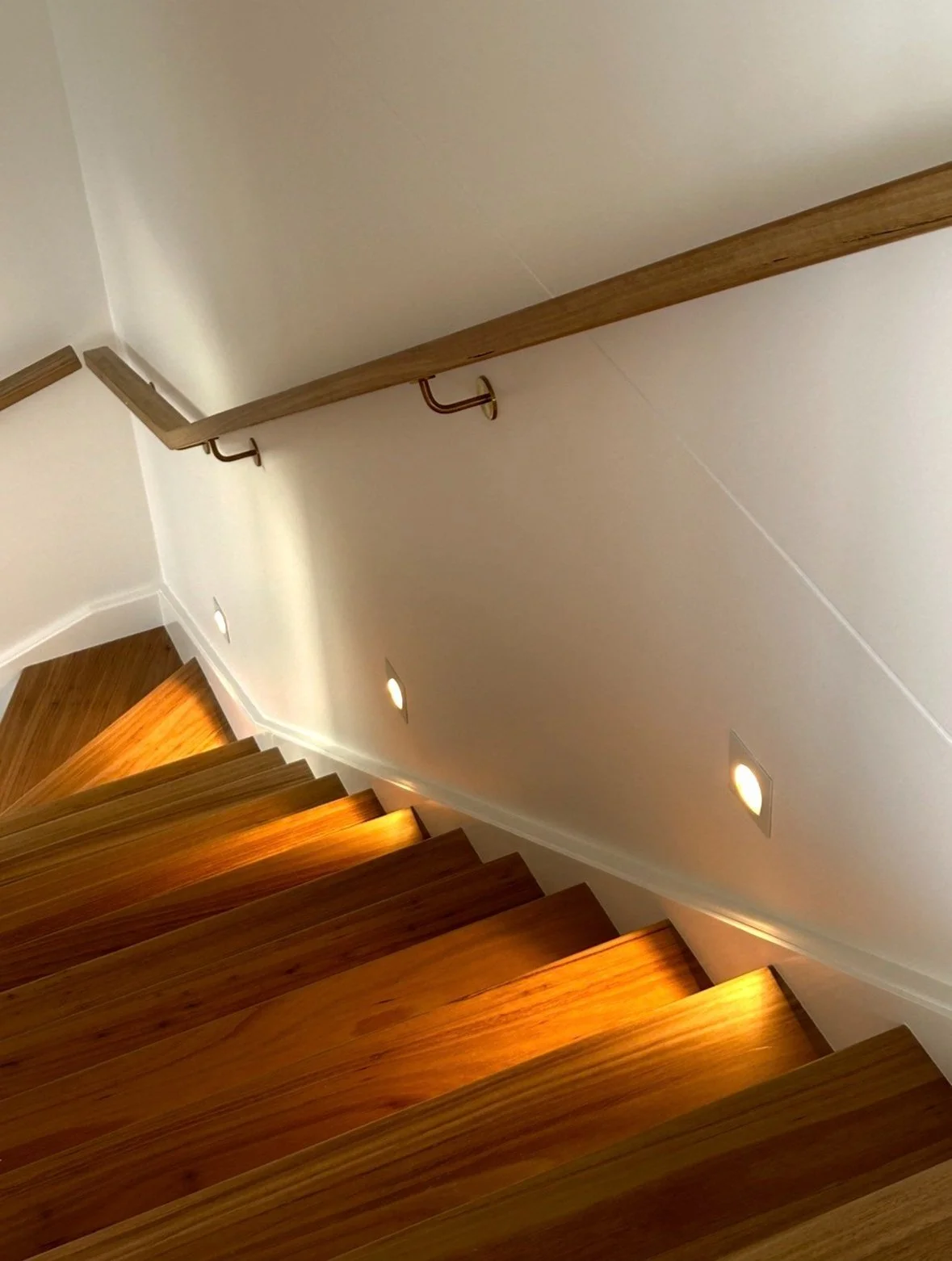 Wooden staircase with wall-mounted lights and handrail
