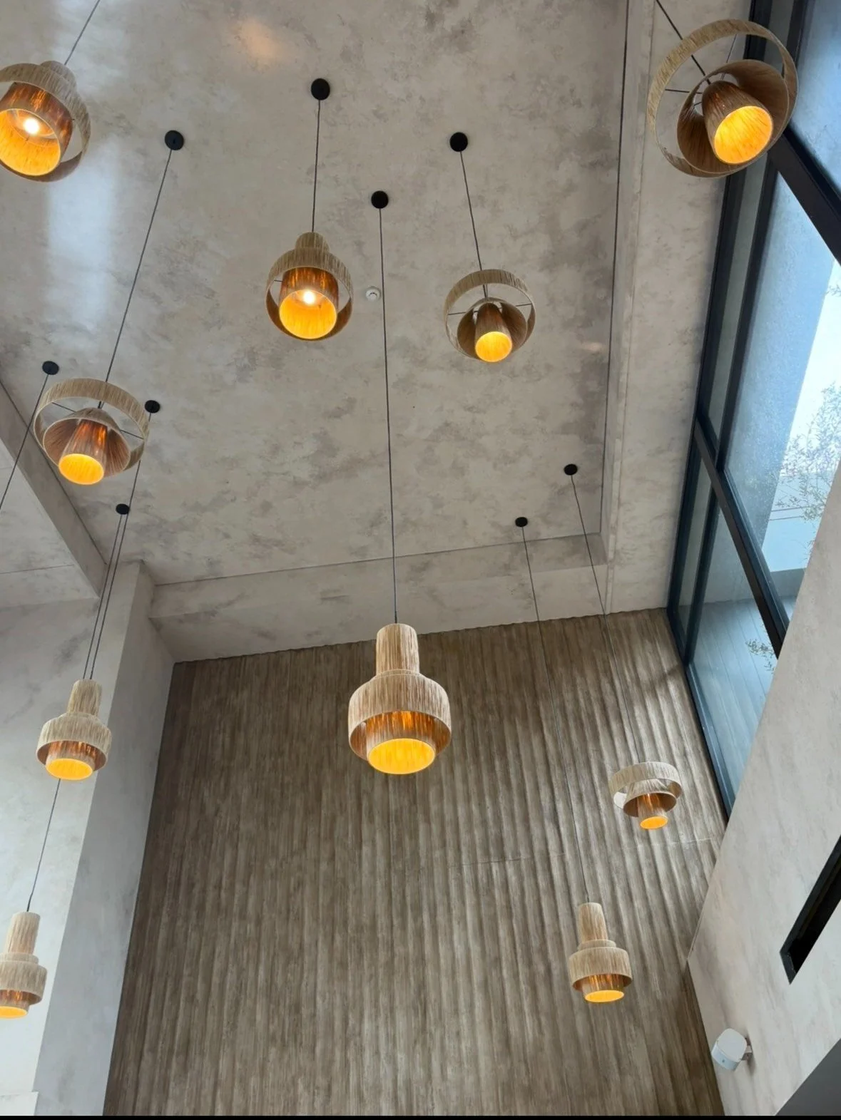 Modern pendant lights hanging from a textured ceiling with a high, large window.
