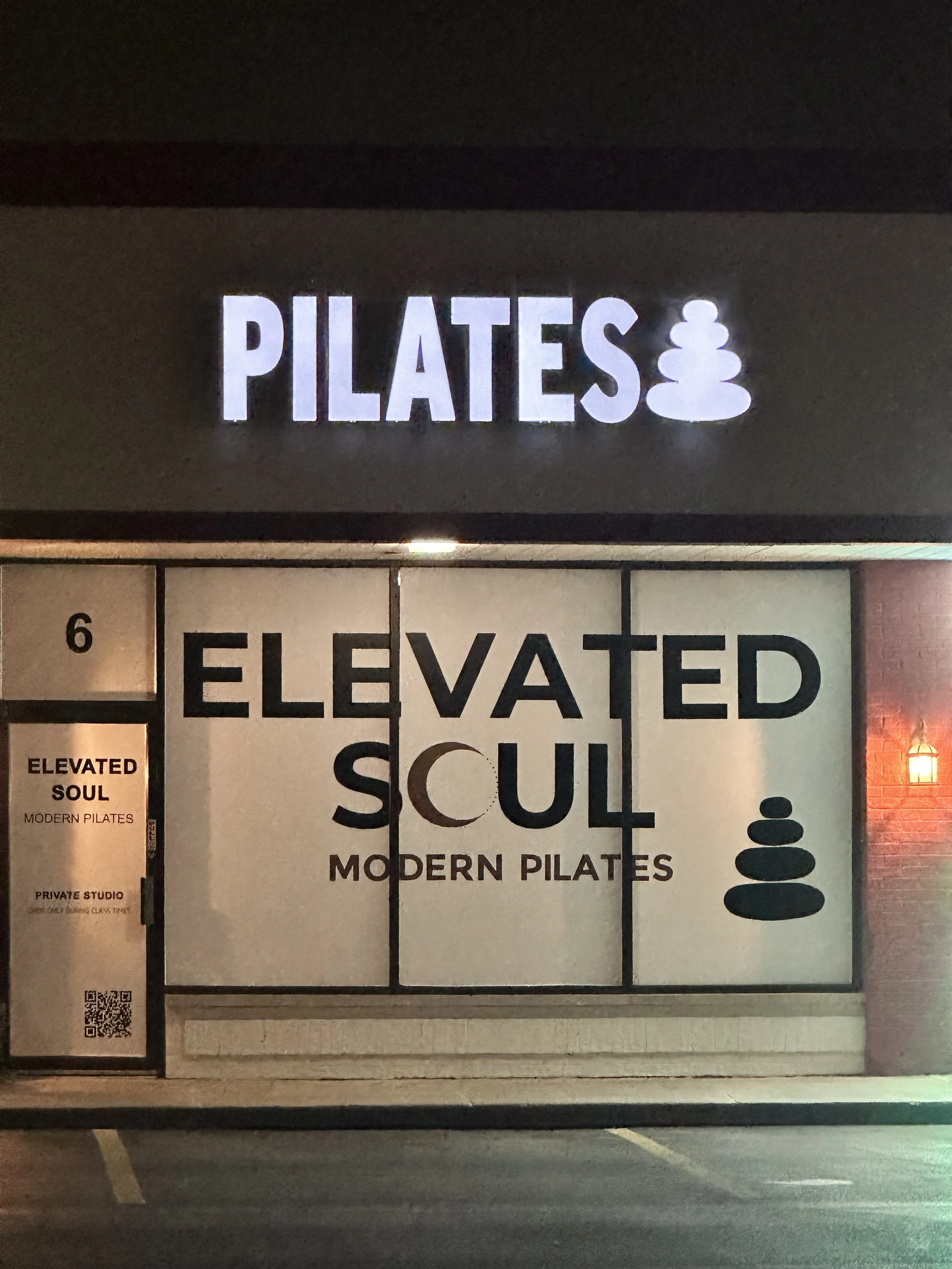 Storefront sign for Pilates and modern Pilates studio with white illuminated sign and black and white graphic of stacked stones.