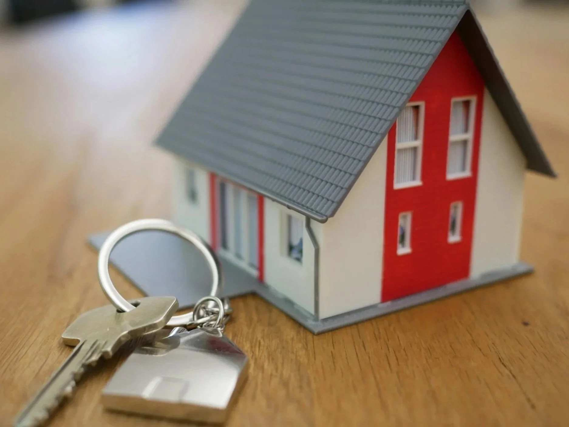 Miniature house and key on wooden surface.
