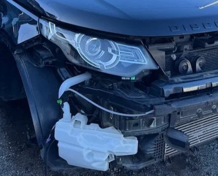 Close-up of the front left side of a Land Rover with the hood open, showing part of the engine and a white windshield washer fluid reservoir